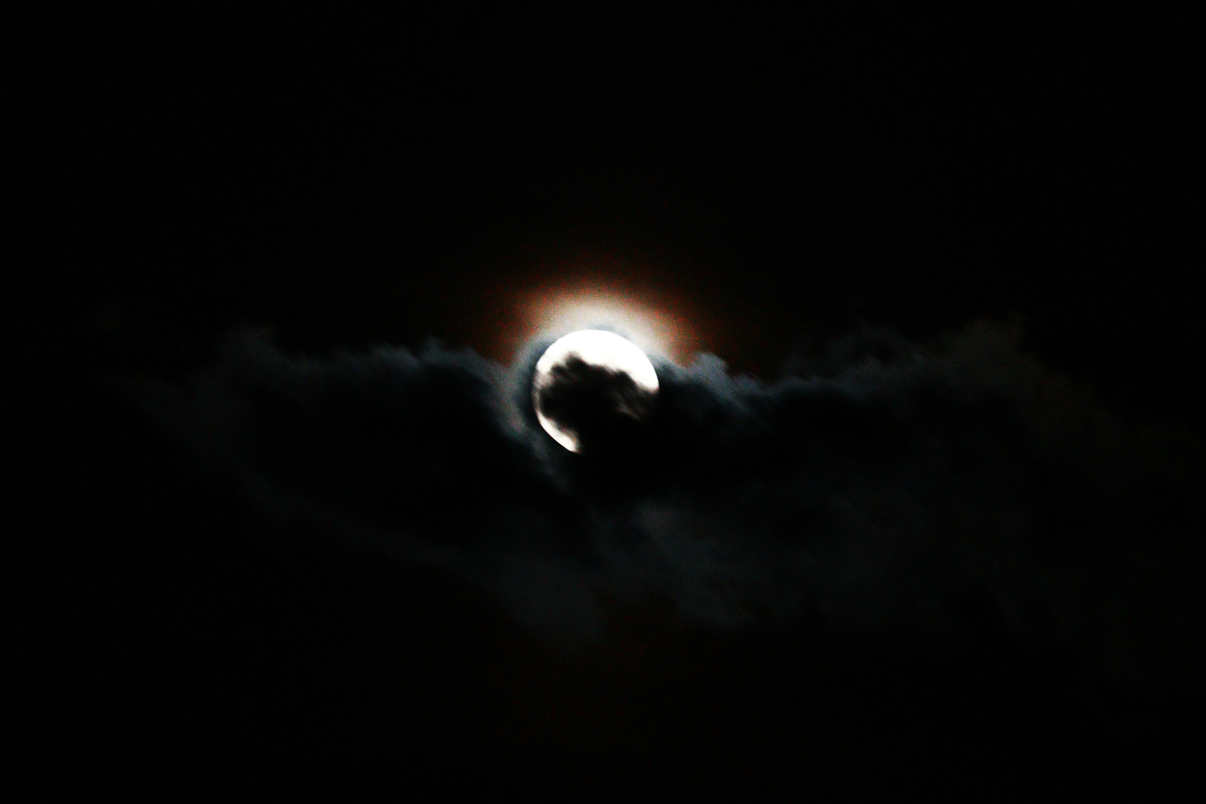 Moon partially obscured by clouds in a dark sky