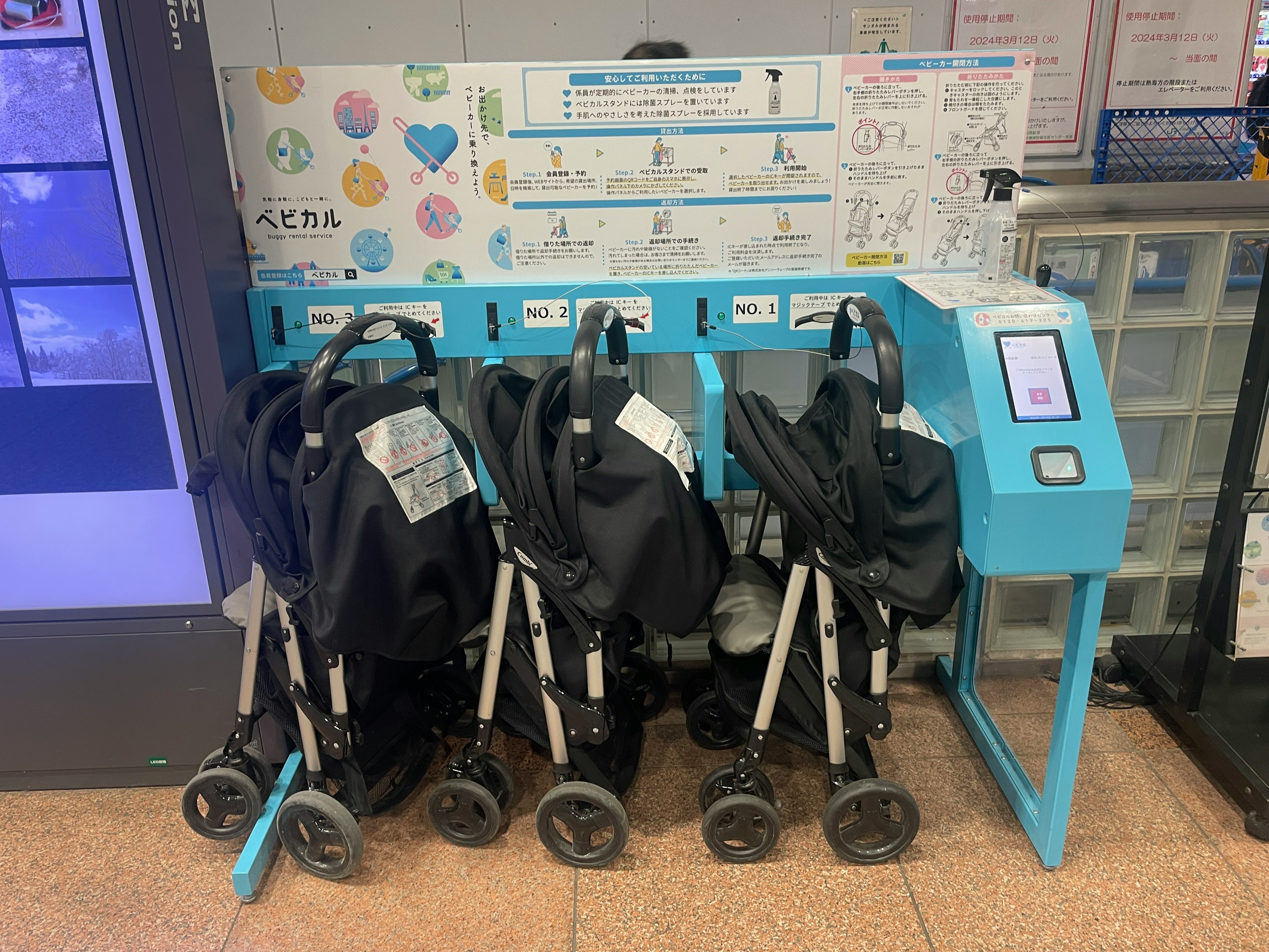 Black strollers lined up at a blue stand with an information panel