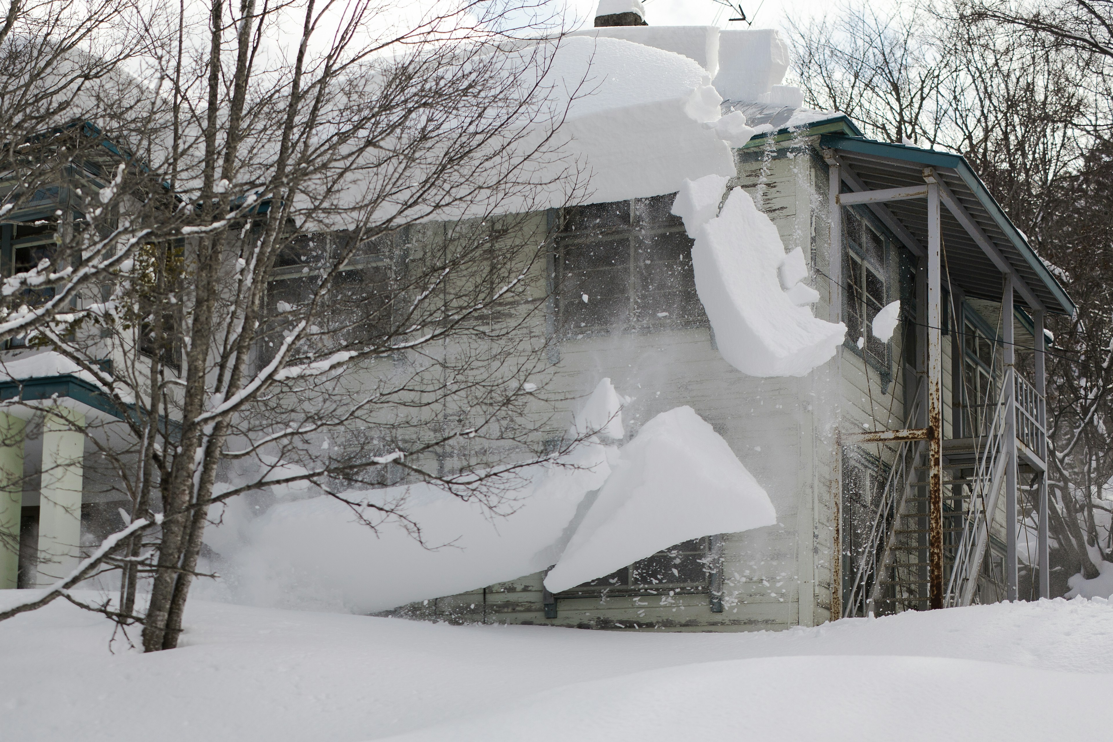 Neige tombant d'un mur d'une maison usée entourée de neige profonde