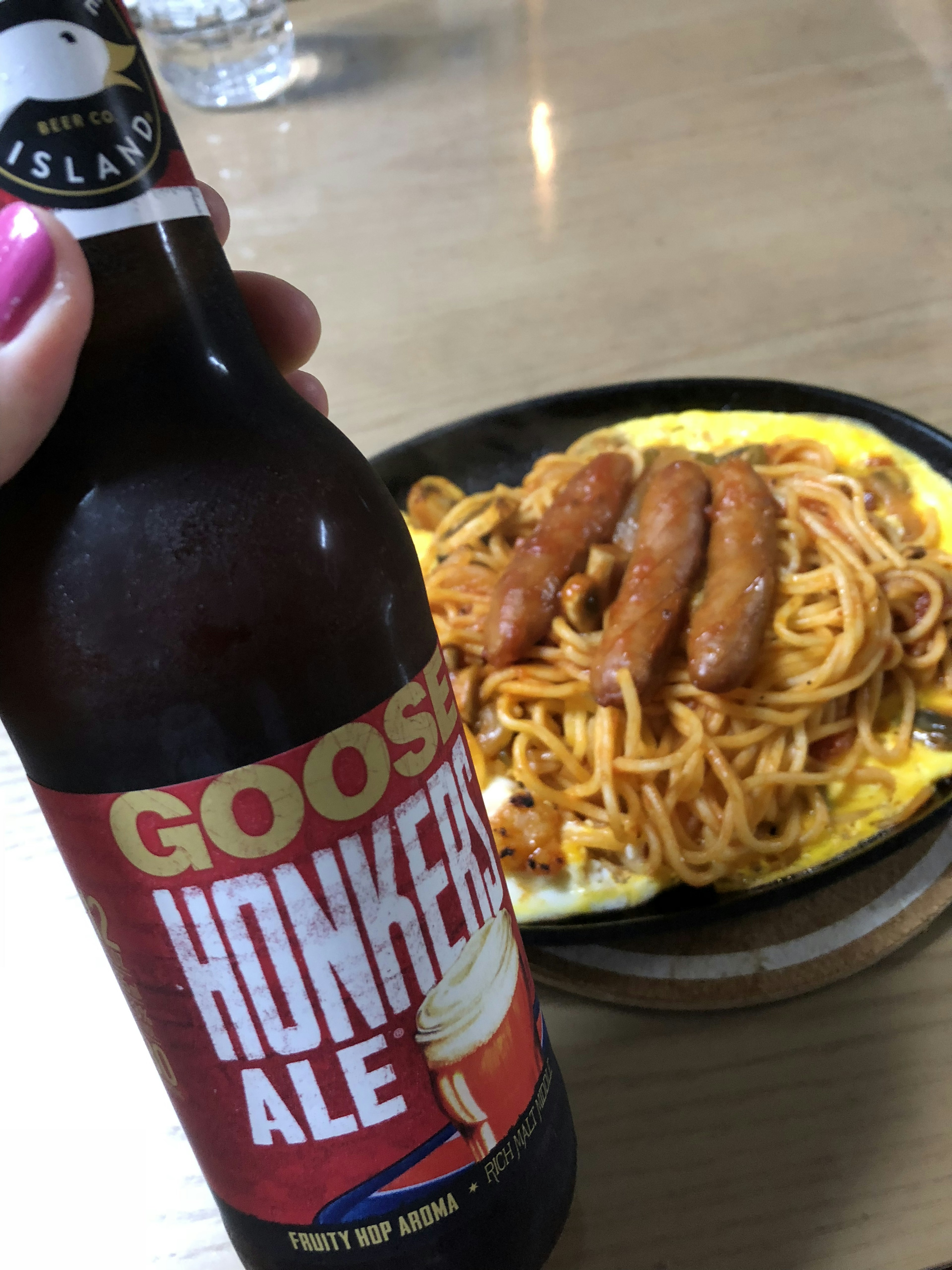 Cerveza Goose Honker's Ale en mano con espaguetis y salchichas en un plato