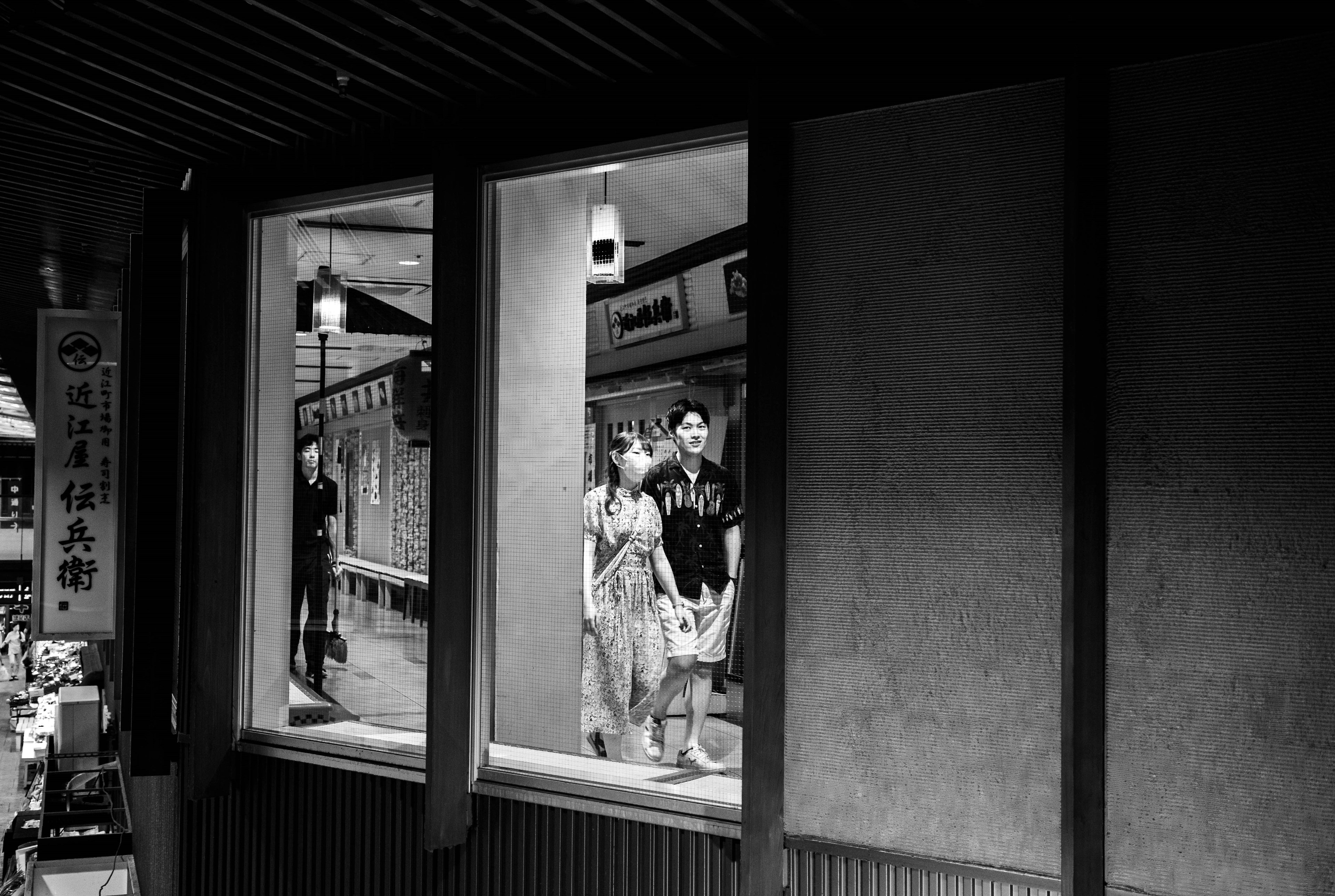 Personas visibles a través de una ventana en una escena de calle en blanco y negro