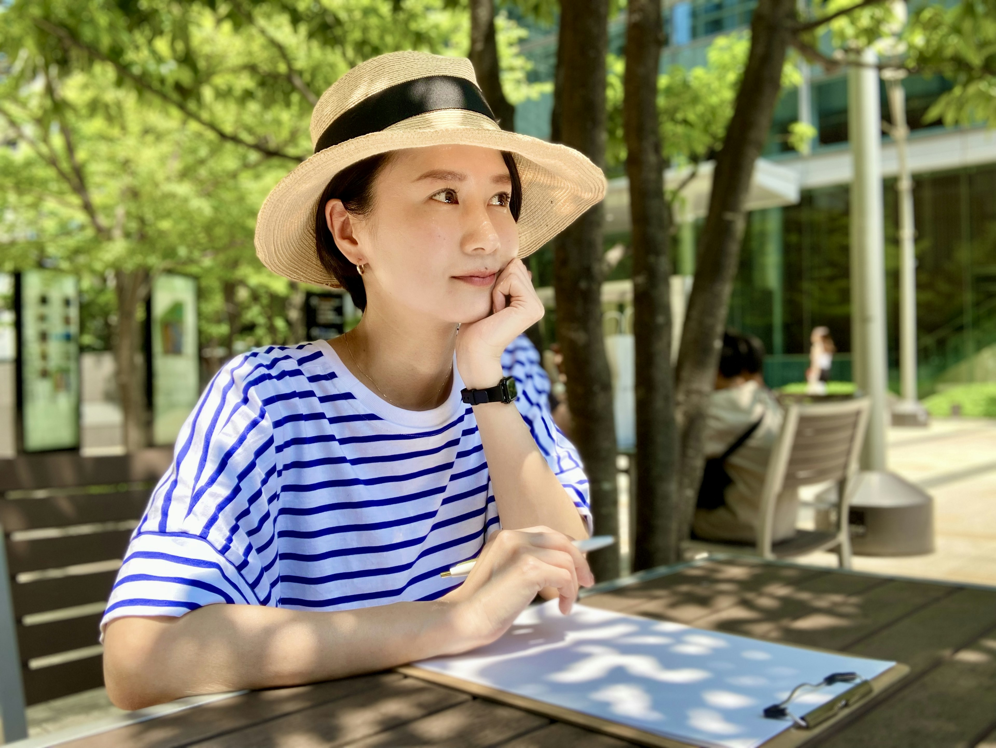 A woman in a striped shirt wearing a hat is thoughtfully resting her chin on her hand