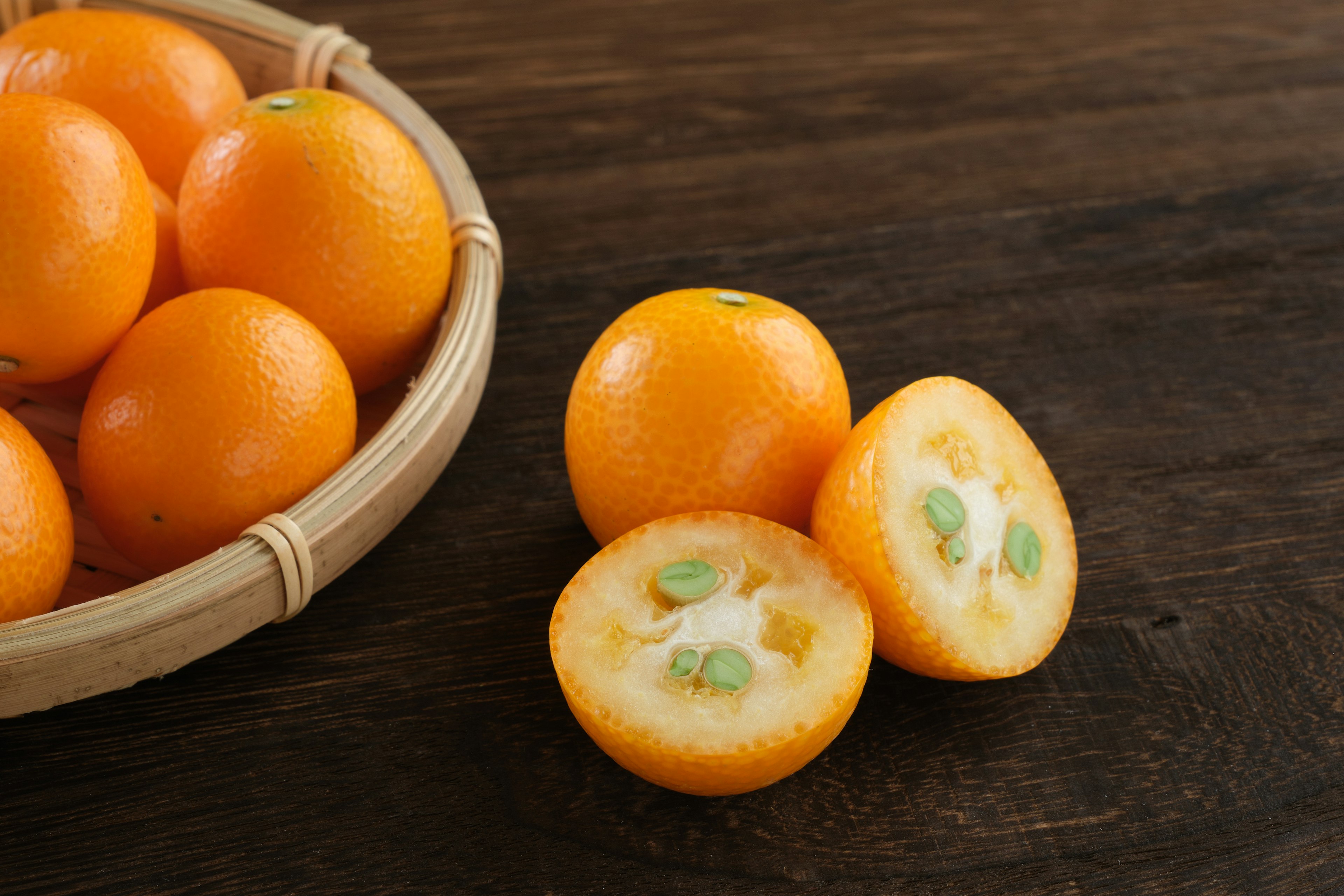 A basket of orange fruits with one fruit cut in half showing its juicy interior