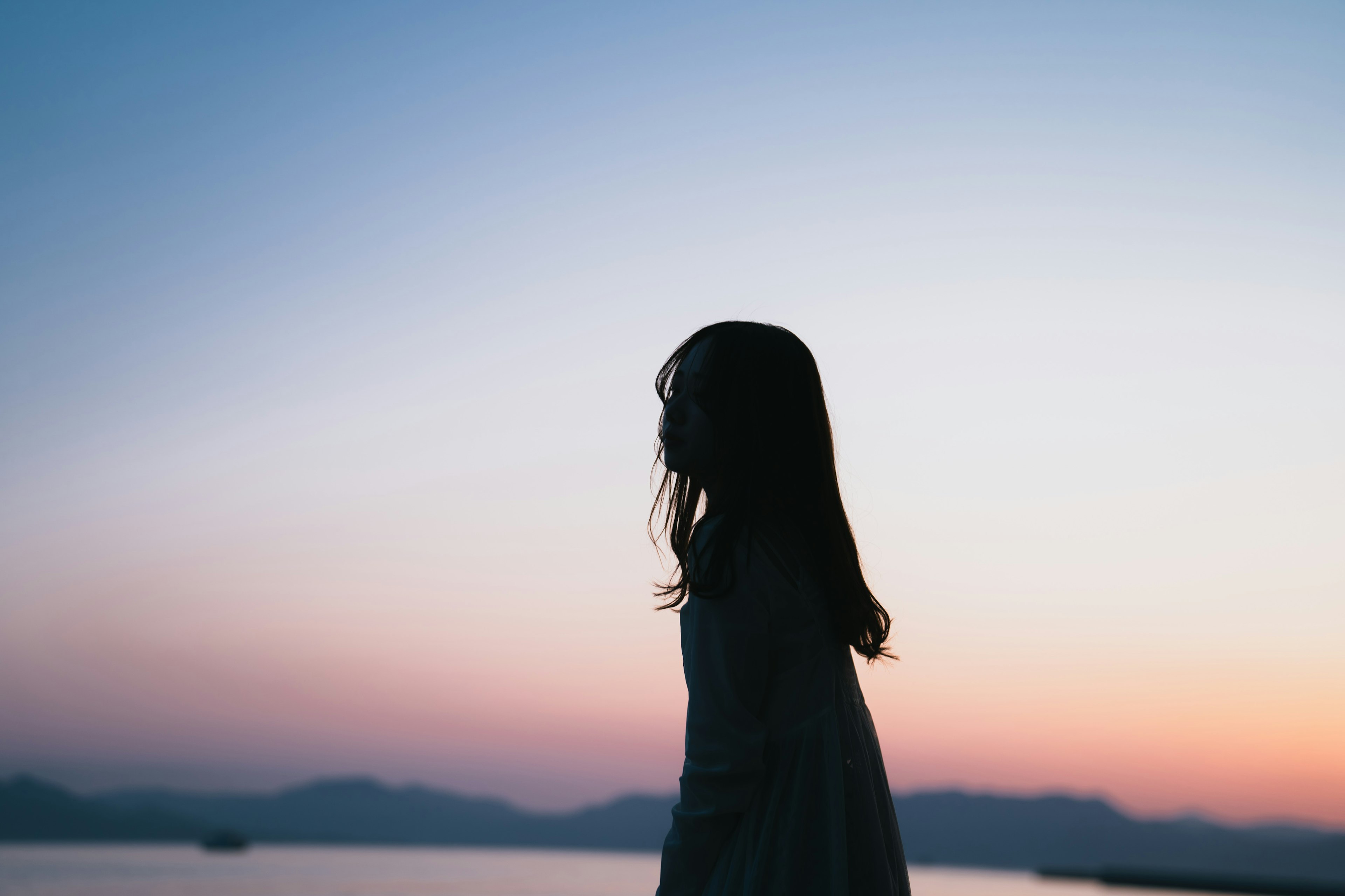 Silhouette einer Frau, die am Meer bei Dämmerung steht