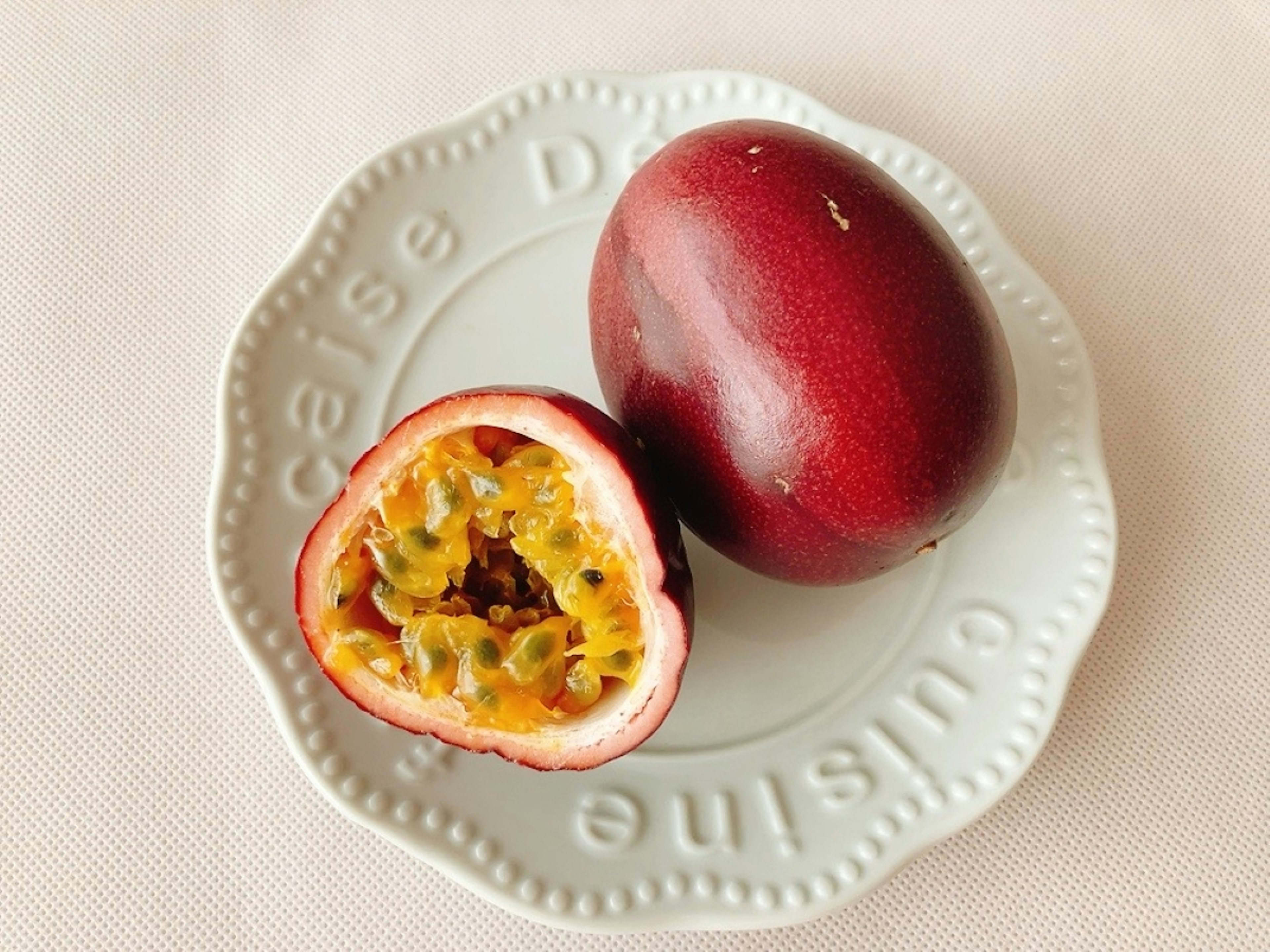 A red passion fruit cut in half on a white plate