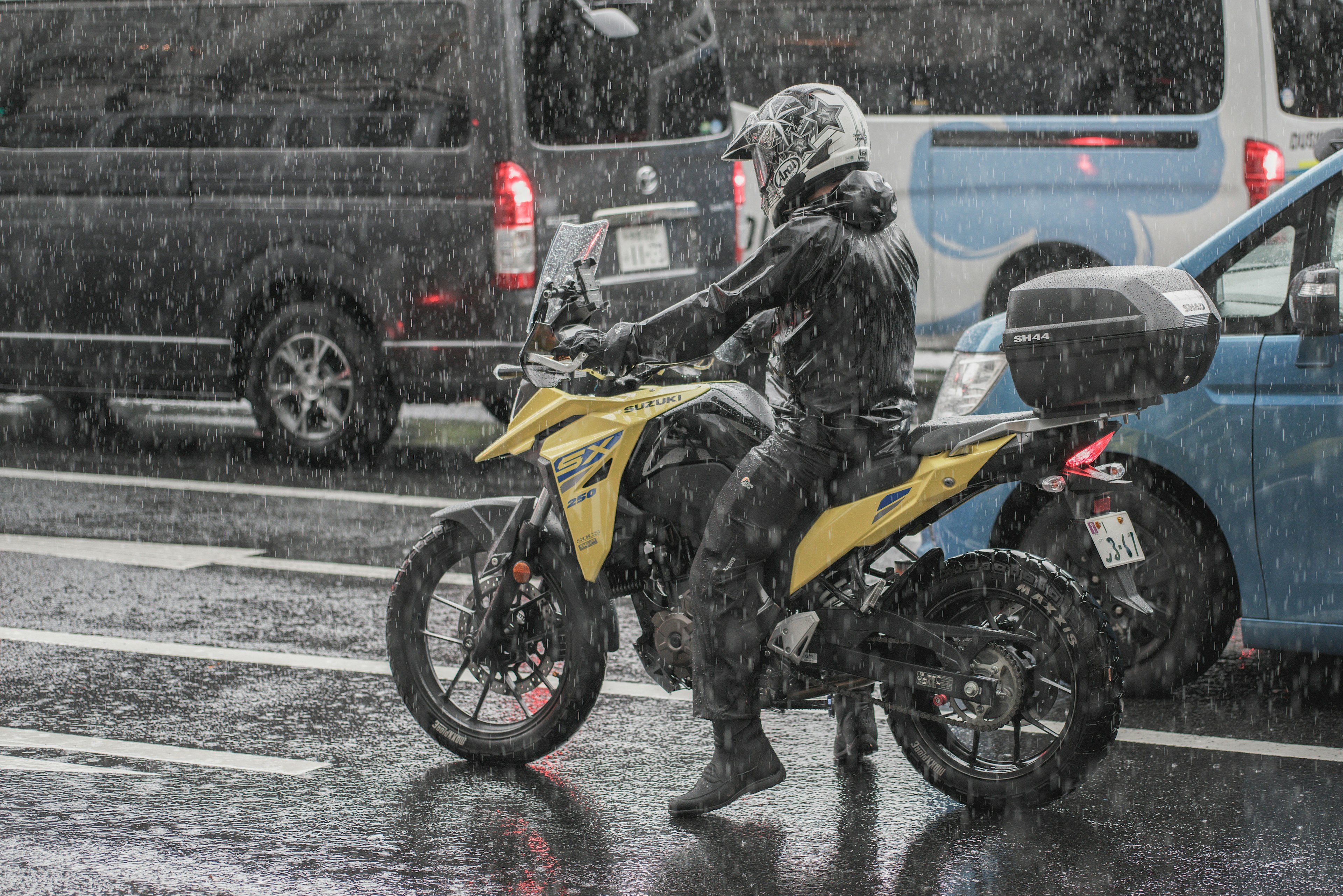 Conductor en una motocicleta amarilla bajo la lluvia con un impermeable negro