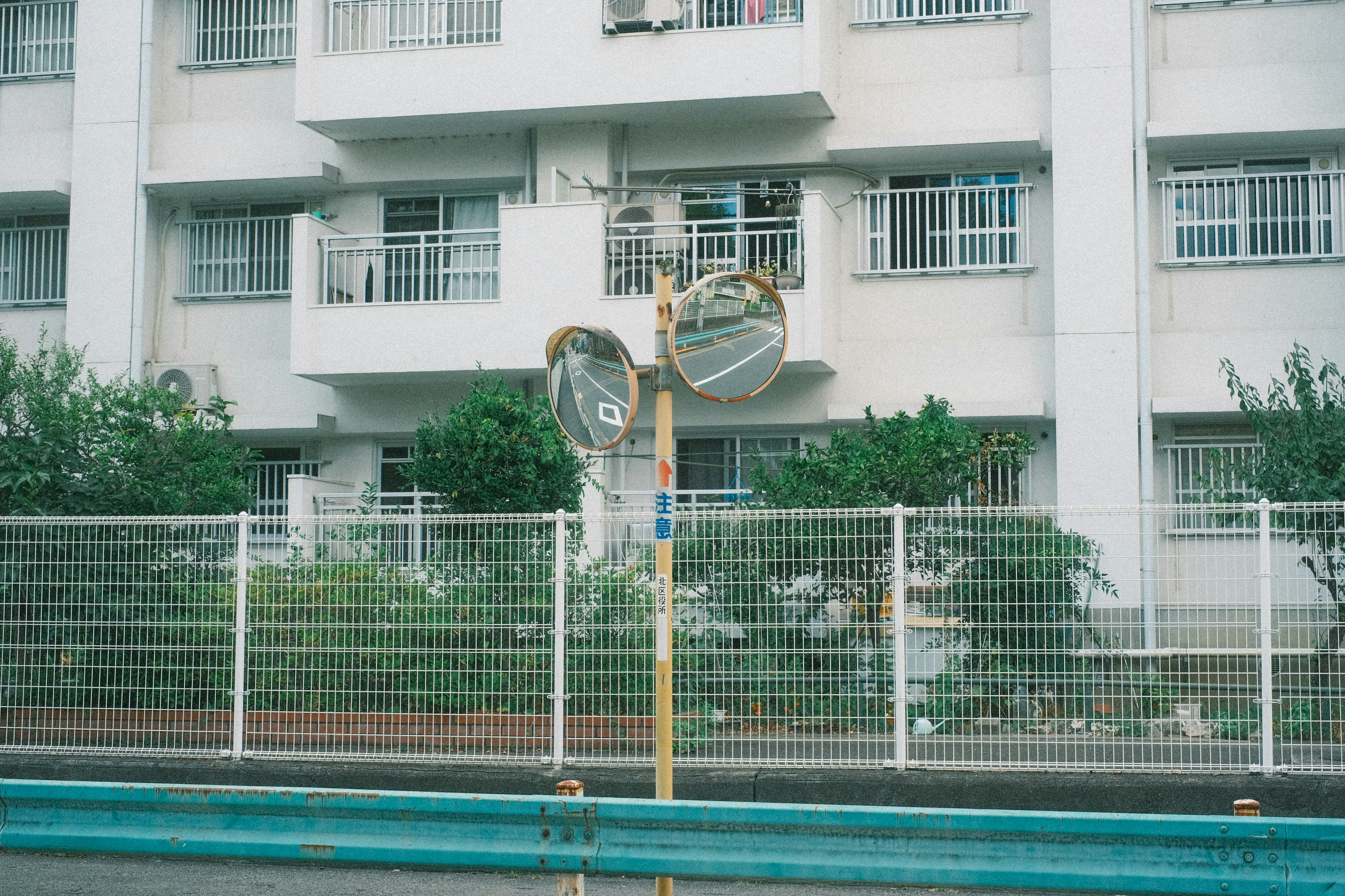 Dos espejos frente a un edificio blanco y una cerca