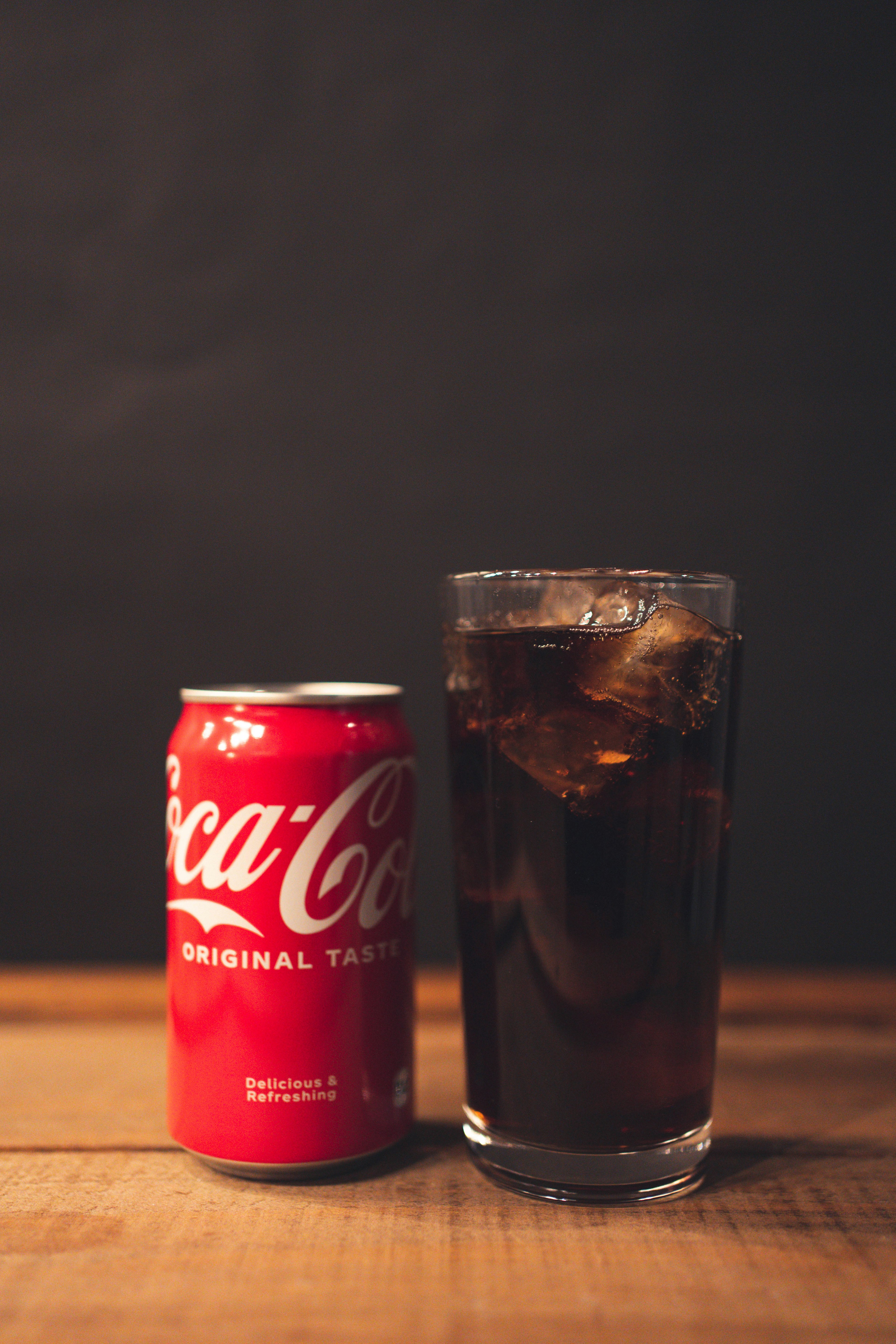 Una lata de Coca-Cola junto a un vaso lleno de hielo y cola