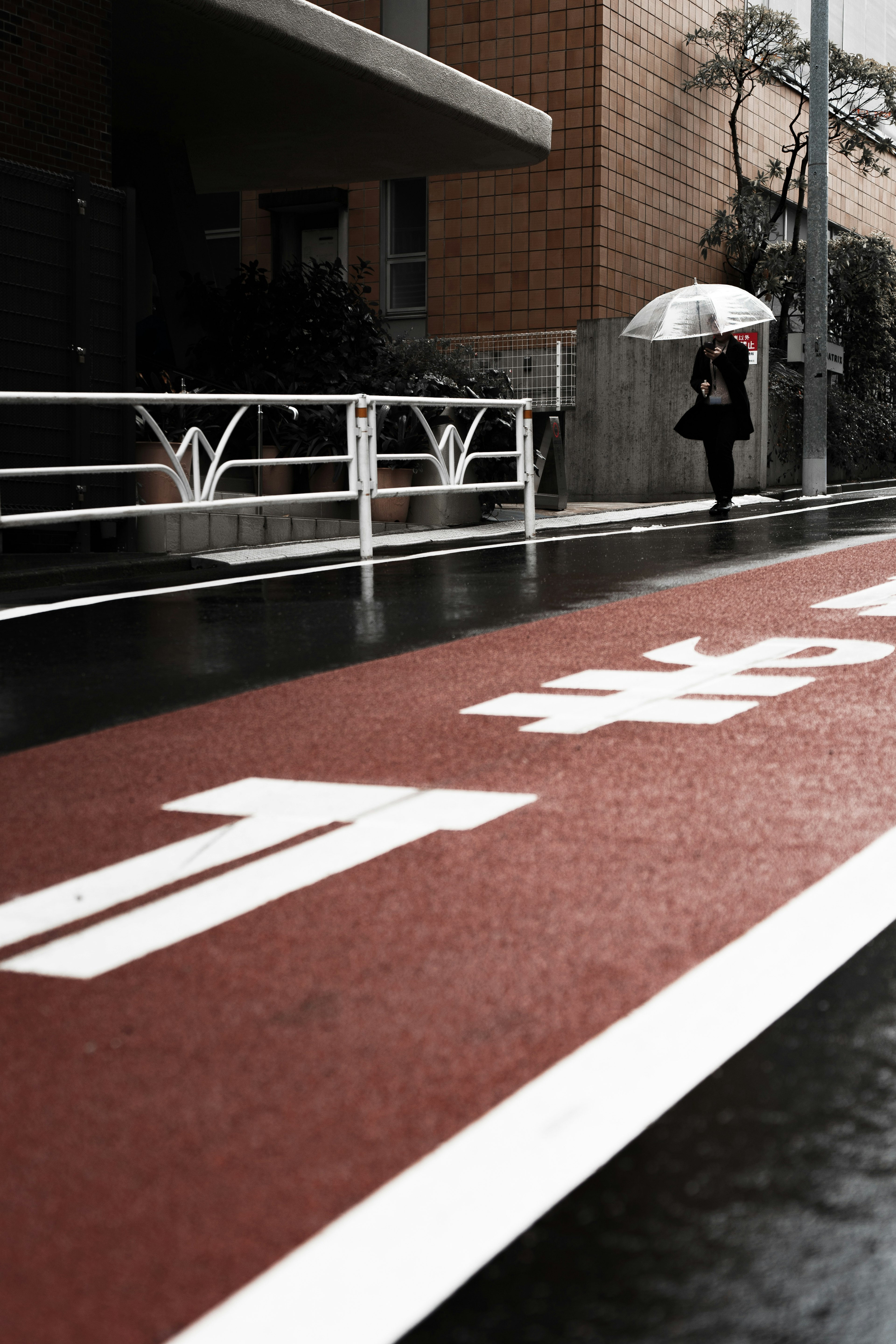 Urban scene featuring a red pathway with white markings a woman walking with an umbrella