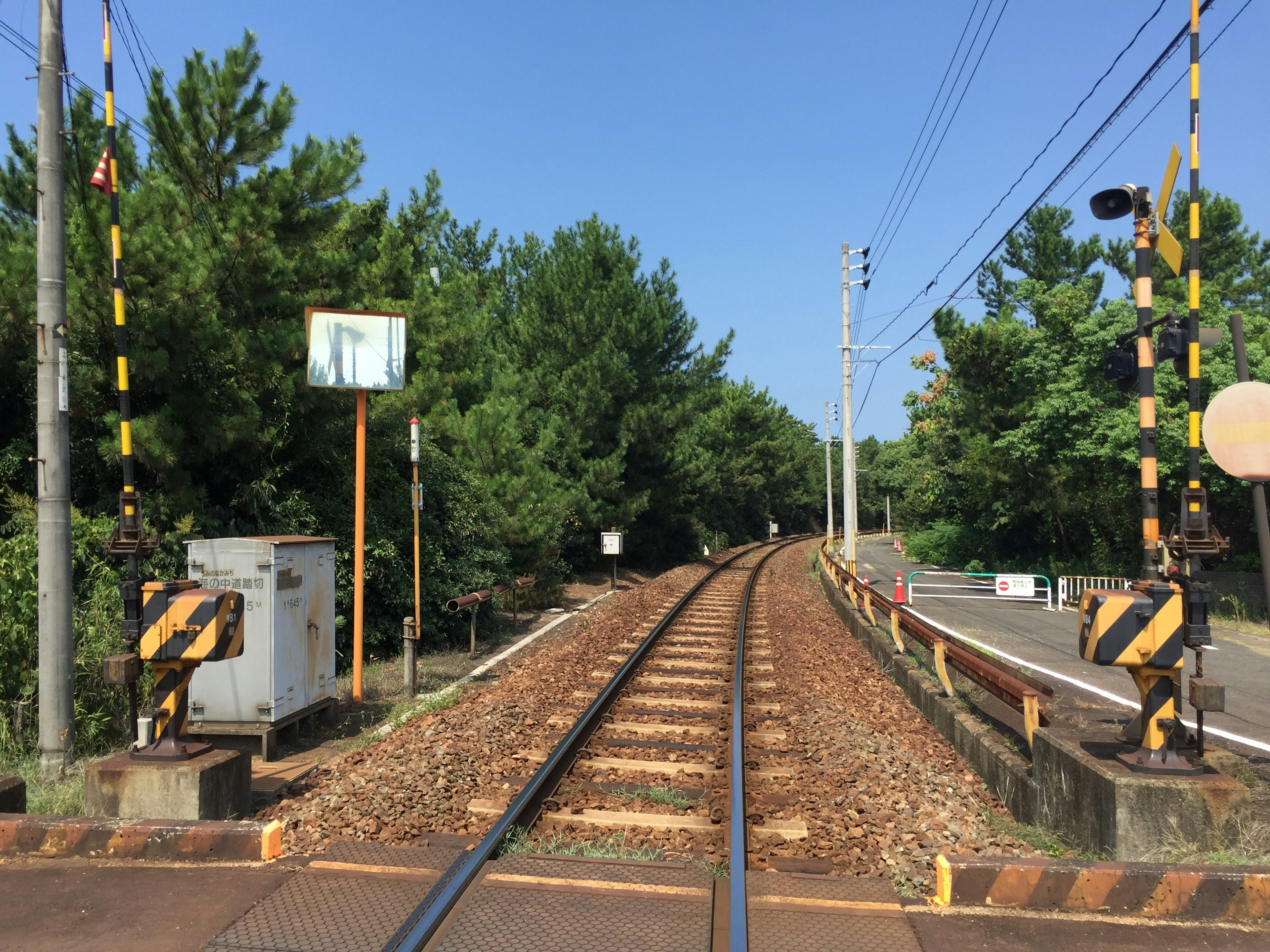 View of railway tracks surrounded by trees with a signal and warning signs