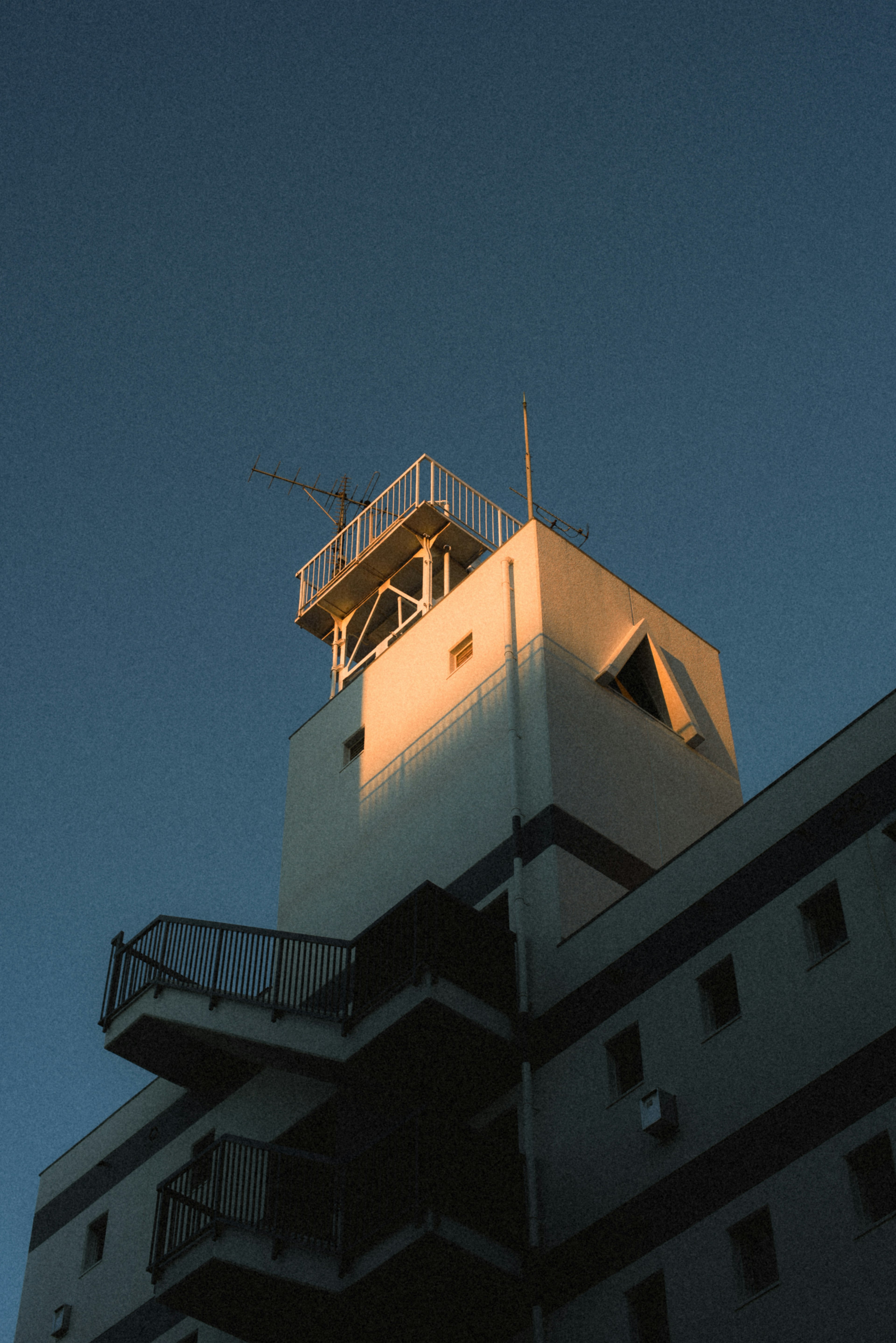 Ein weißer Gebäudeturm unter einem blauen Himmel, beleuchtet vom Sonnenuntergang