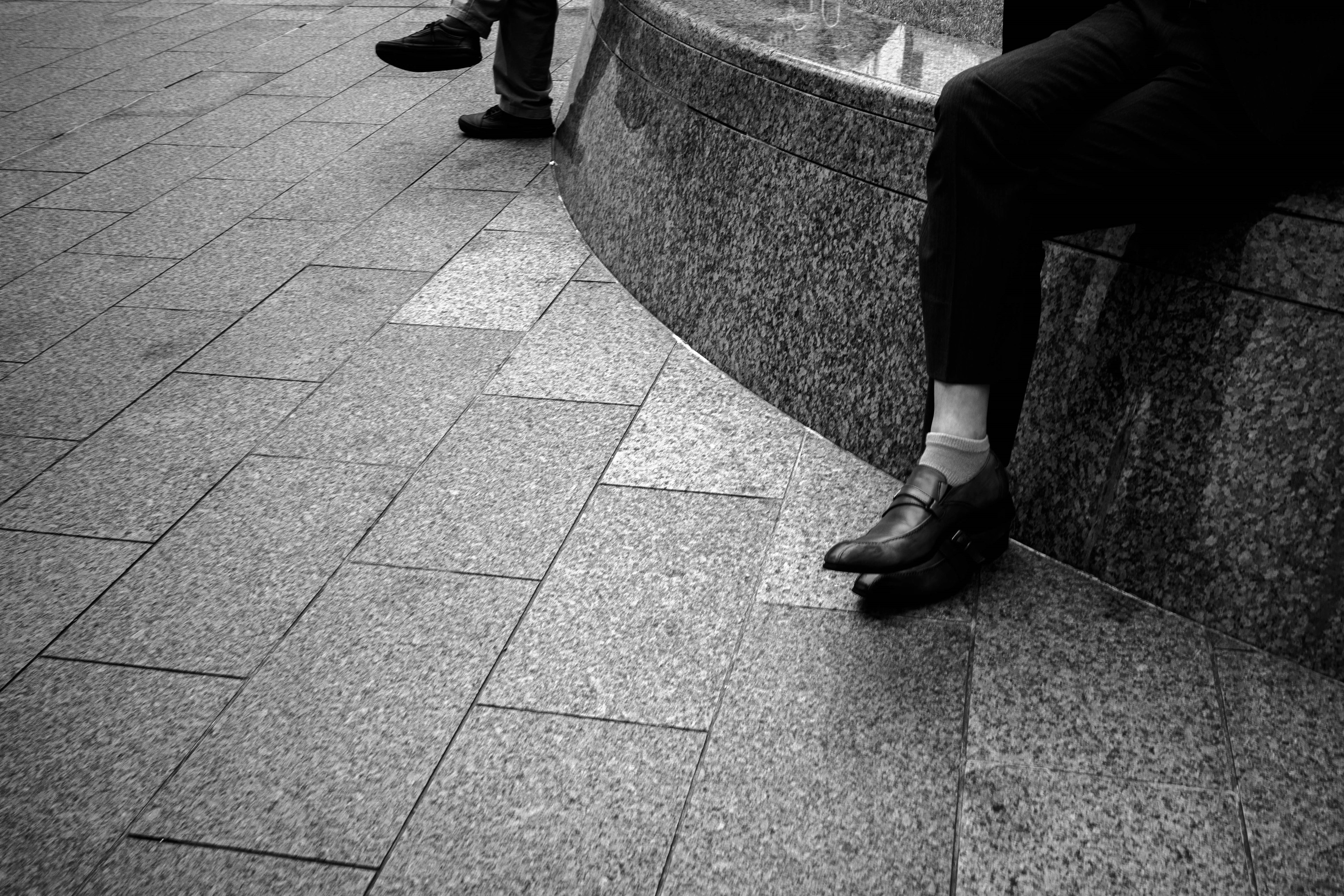 Black and white photograph showing two men's feet resting on a curved stone bench