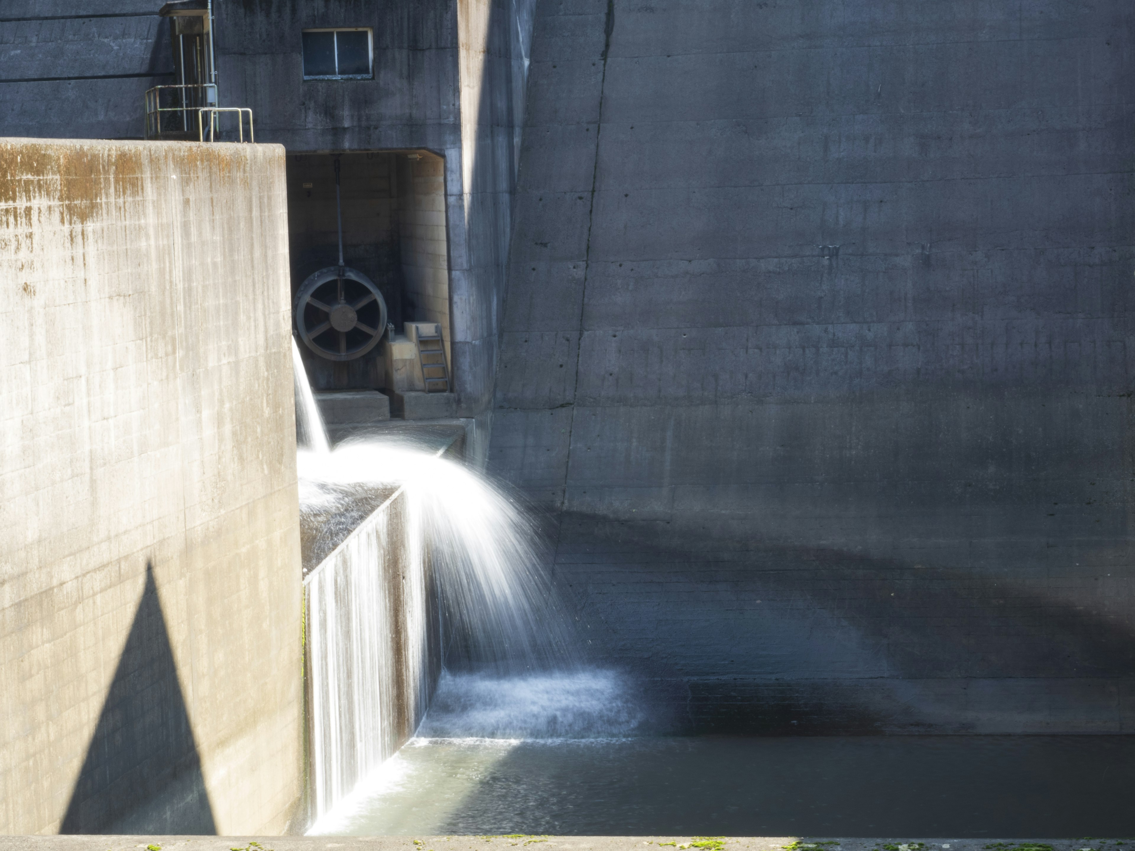 Water flowing from a concrete structure with industrial elements in the background