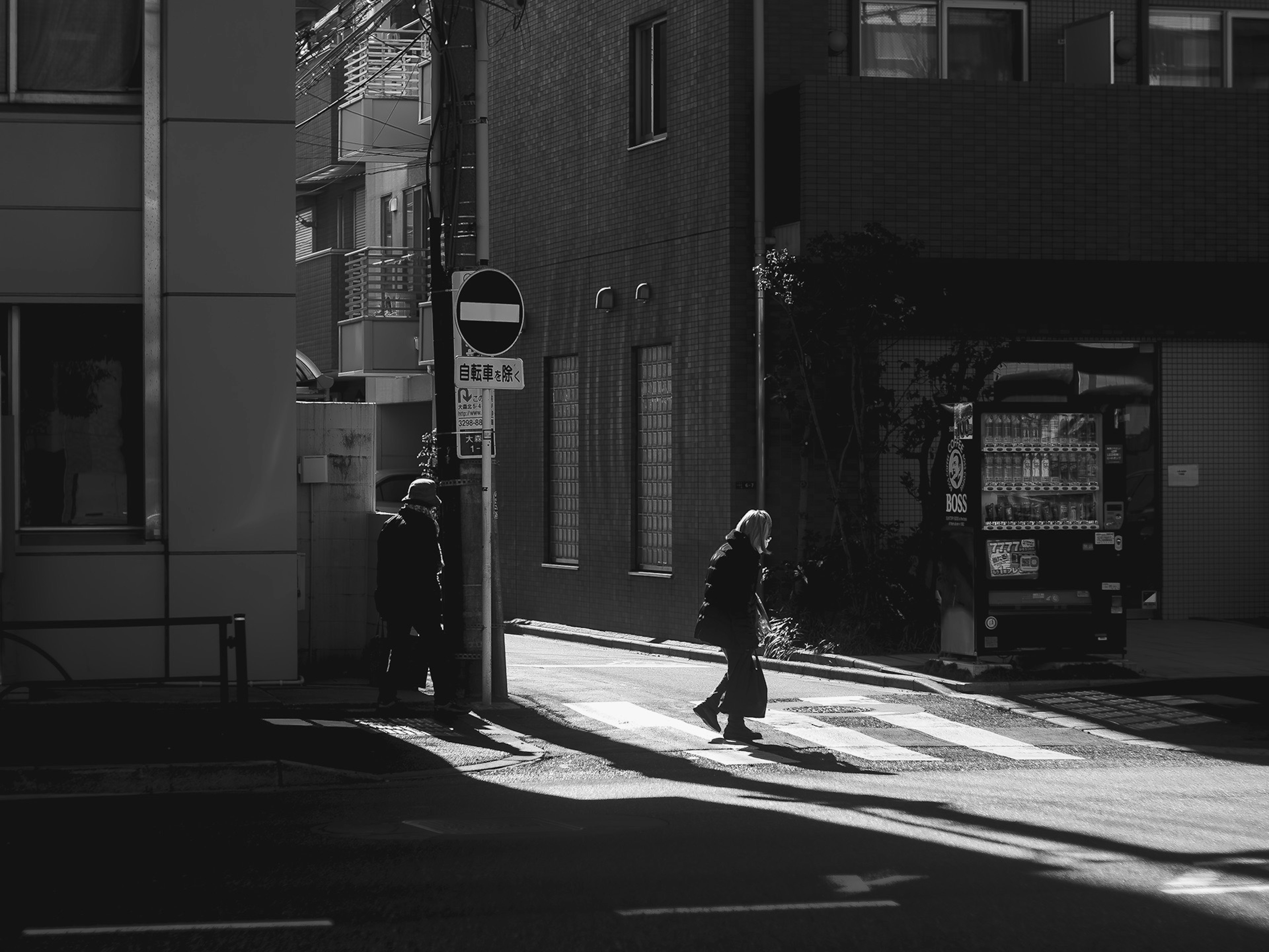 Persone che camminano all'angolo di una città con luce e ombra su un attraversamento pedonale