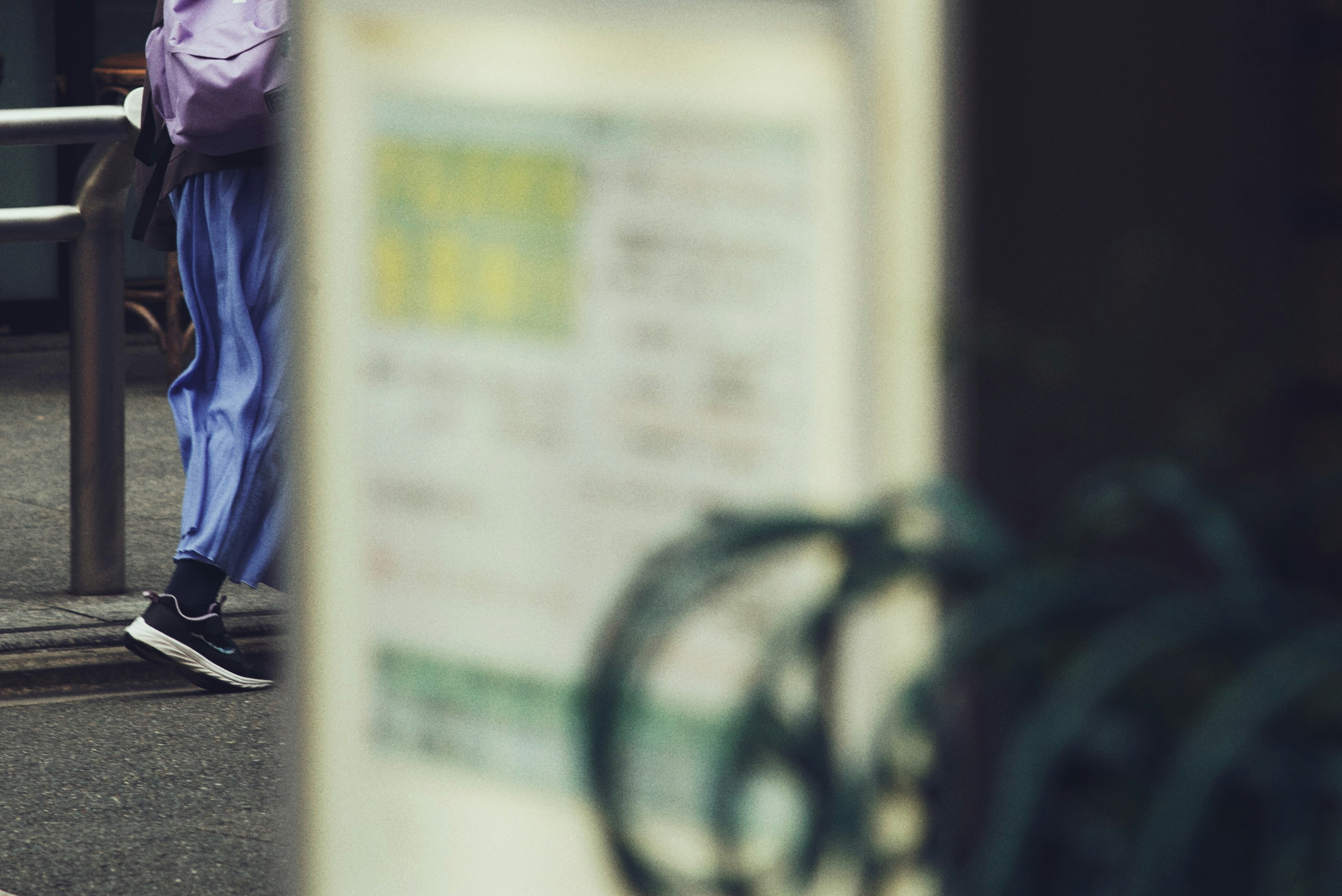 A person walking past a train station entrance with partial view of a sign