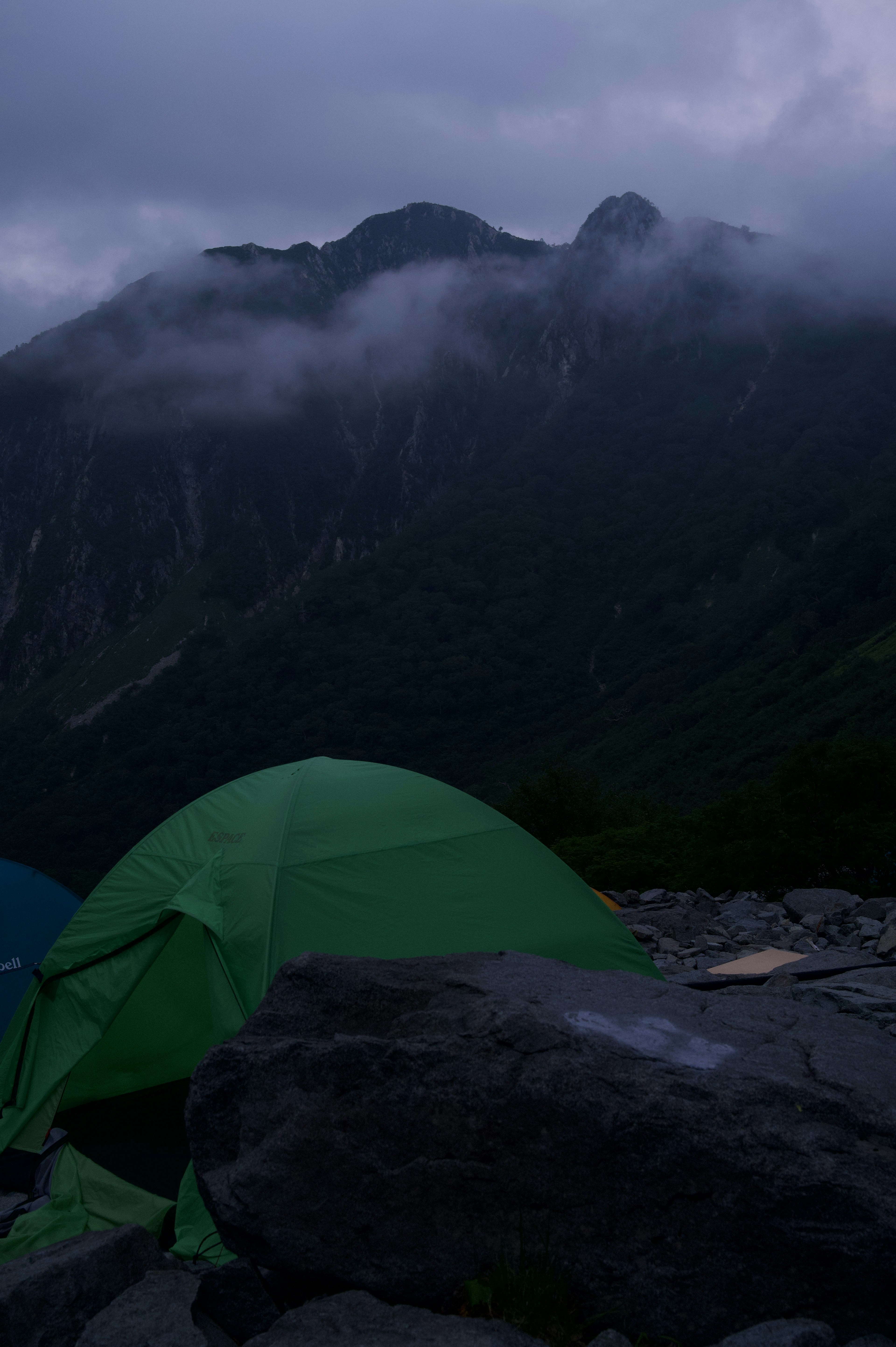 霧のかかった山の背景にある緑のテントと岩