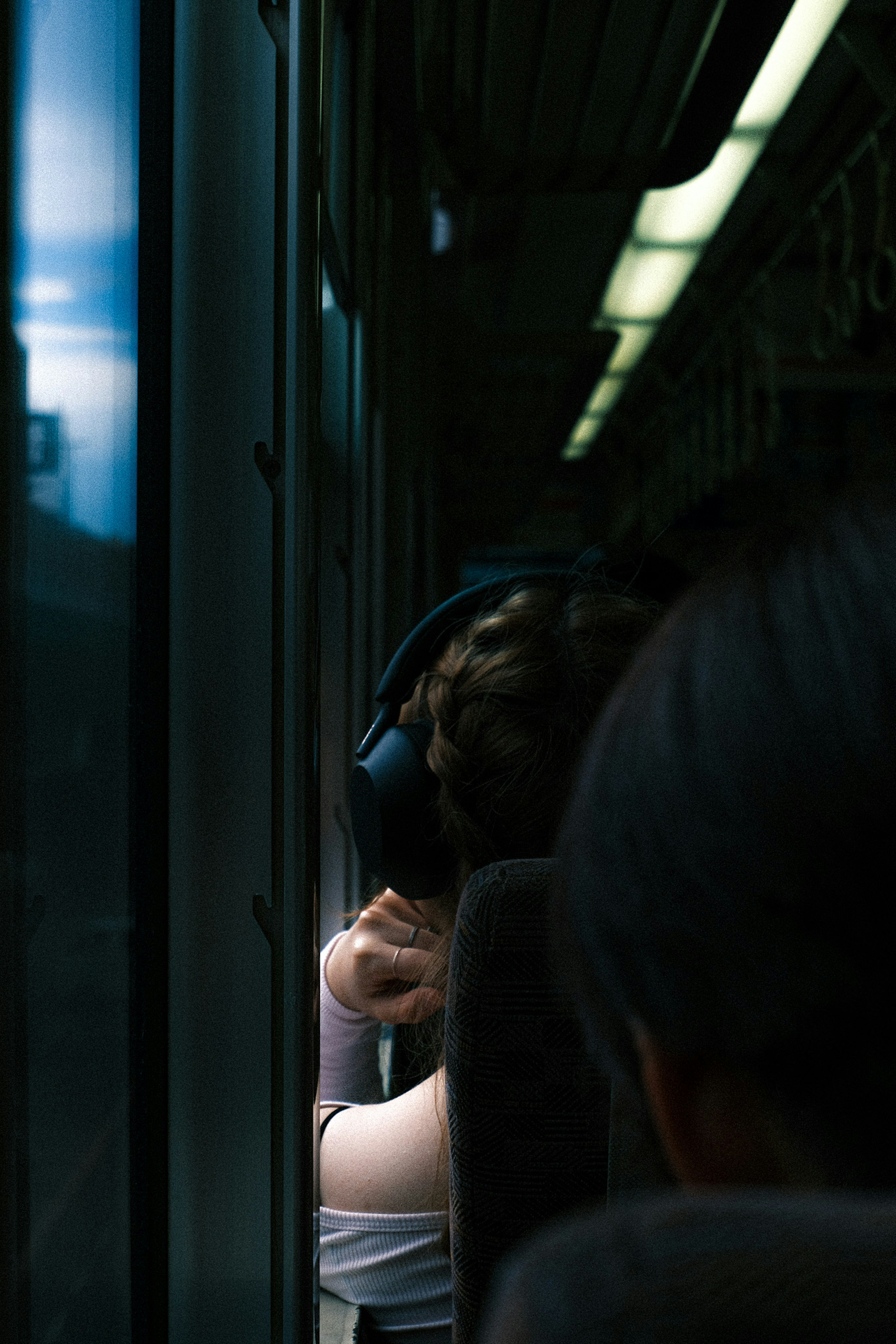 A woman sitting by the window on a train wearing headphones and looking outside