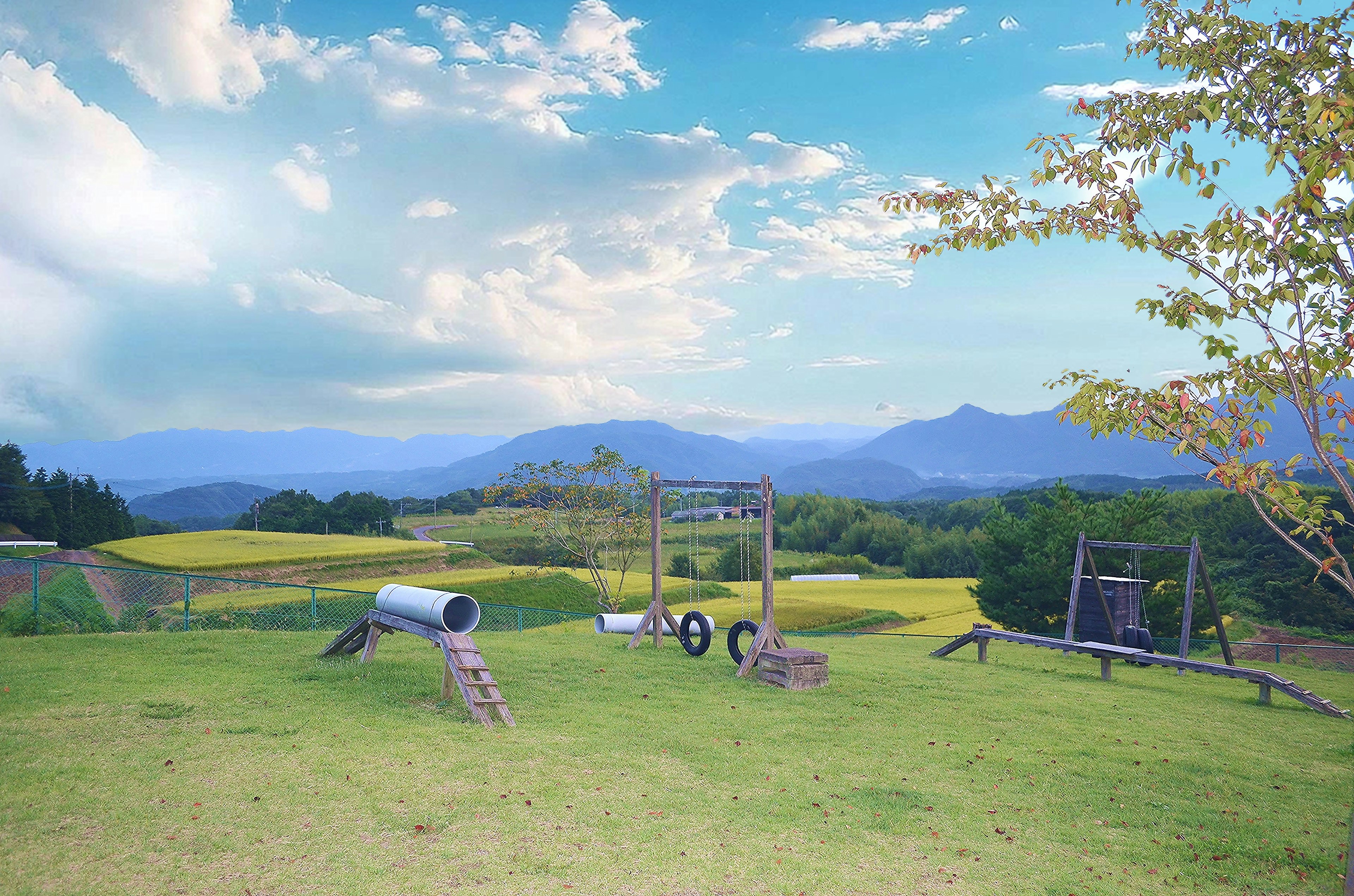 A scenic playground with swings and climbing structures against a backdrop of mountains and blue sky