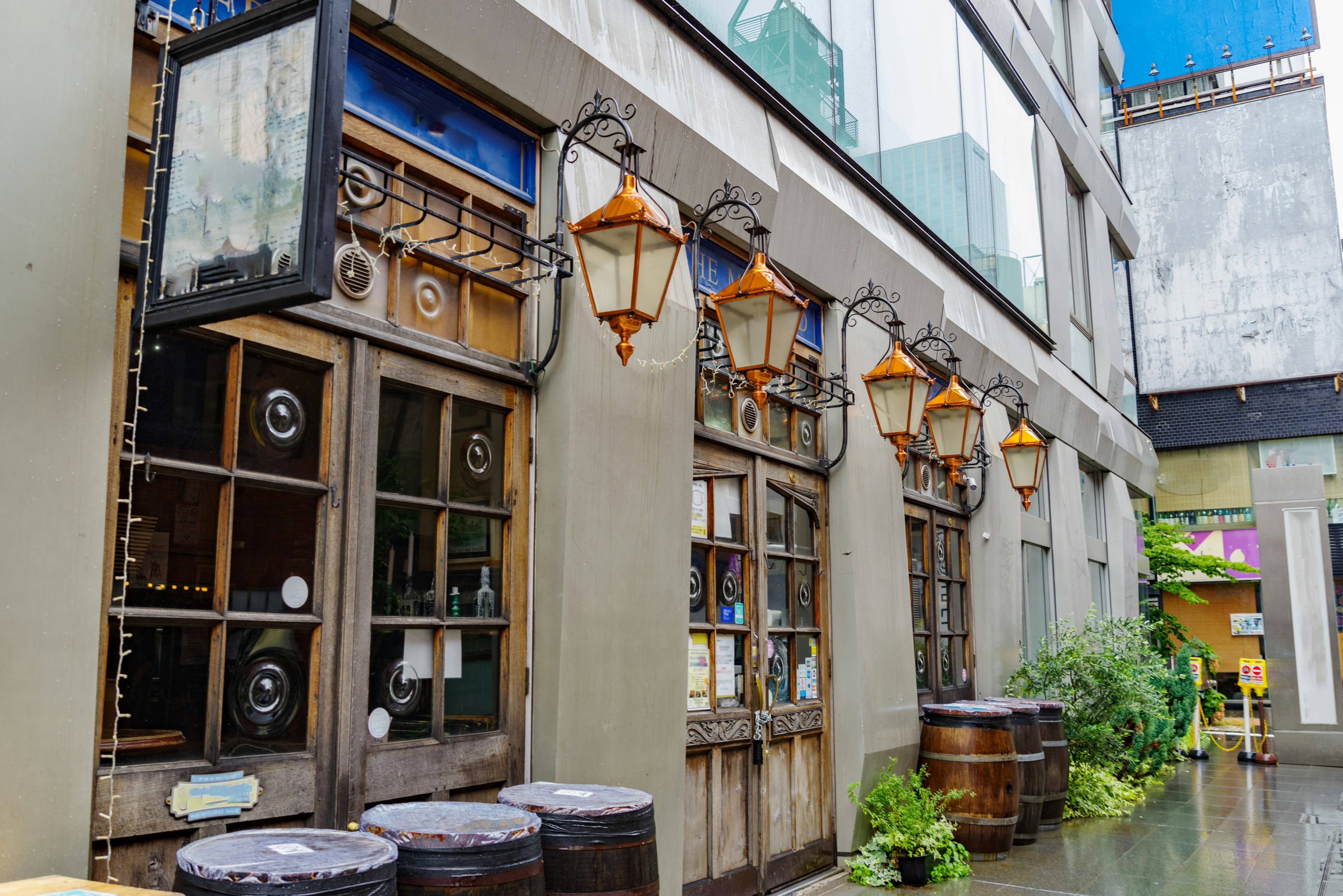 Eingang eines Retro-Cafés mit Holztüren und orangefarbenen Laternen in einer regnerischen Gasse