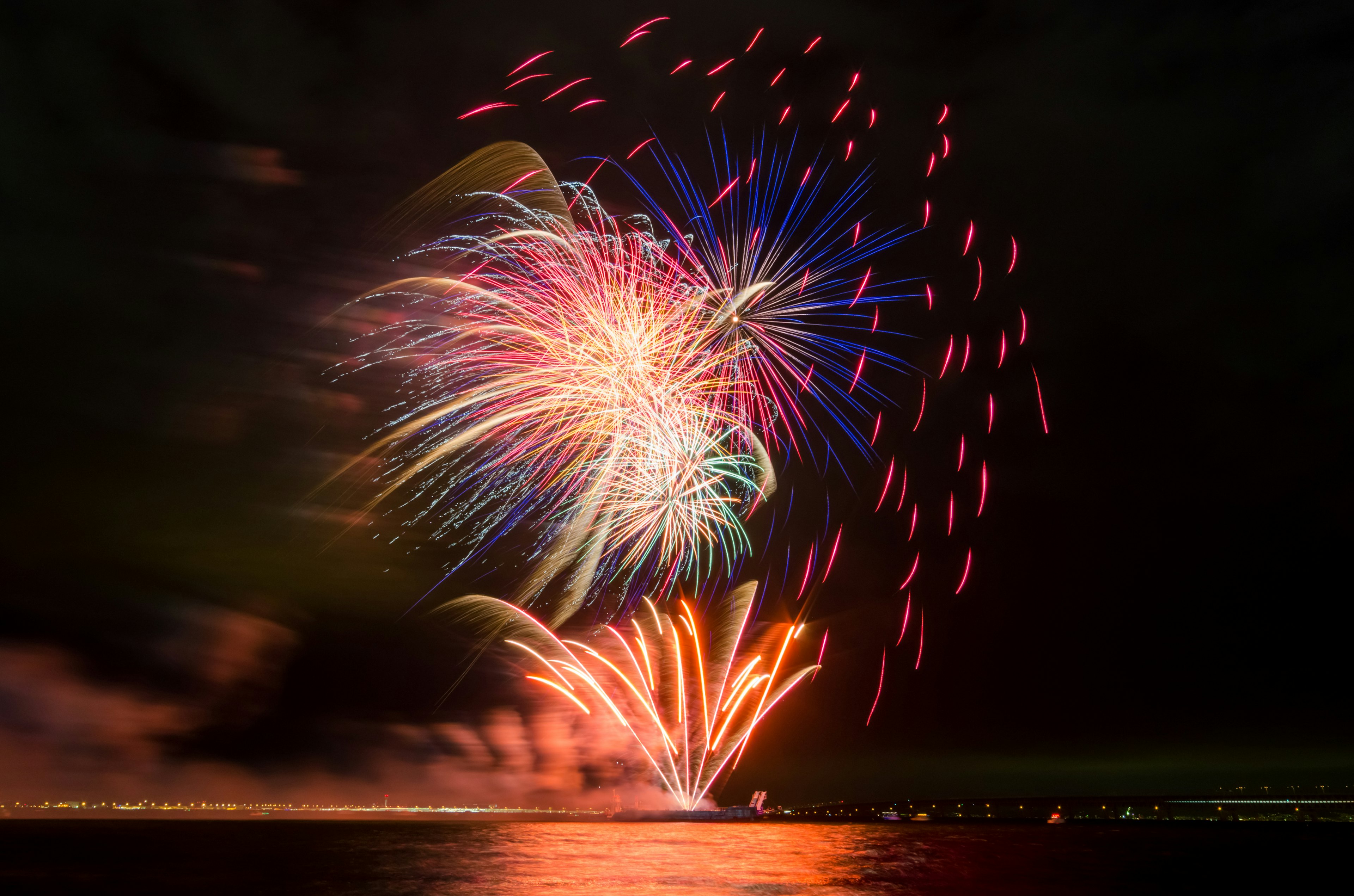 Fuochi d'artificio colorati che esplodono nel cielo notturno riflettendosi sull'acqua