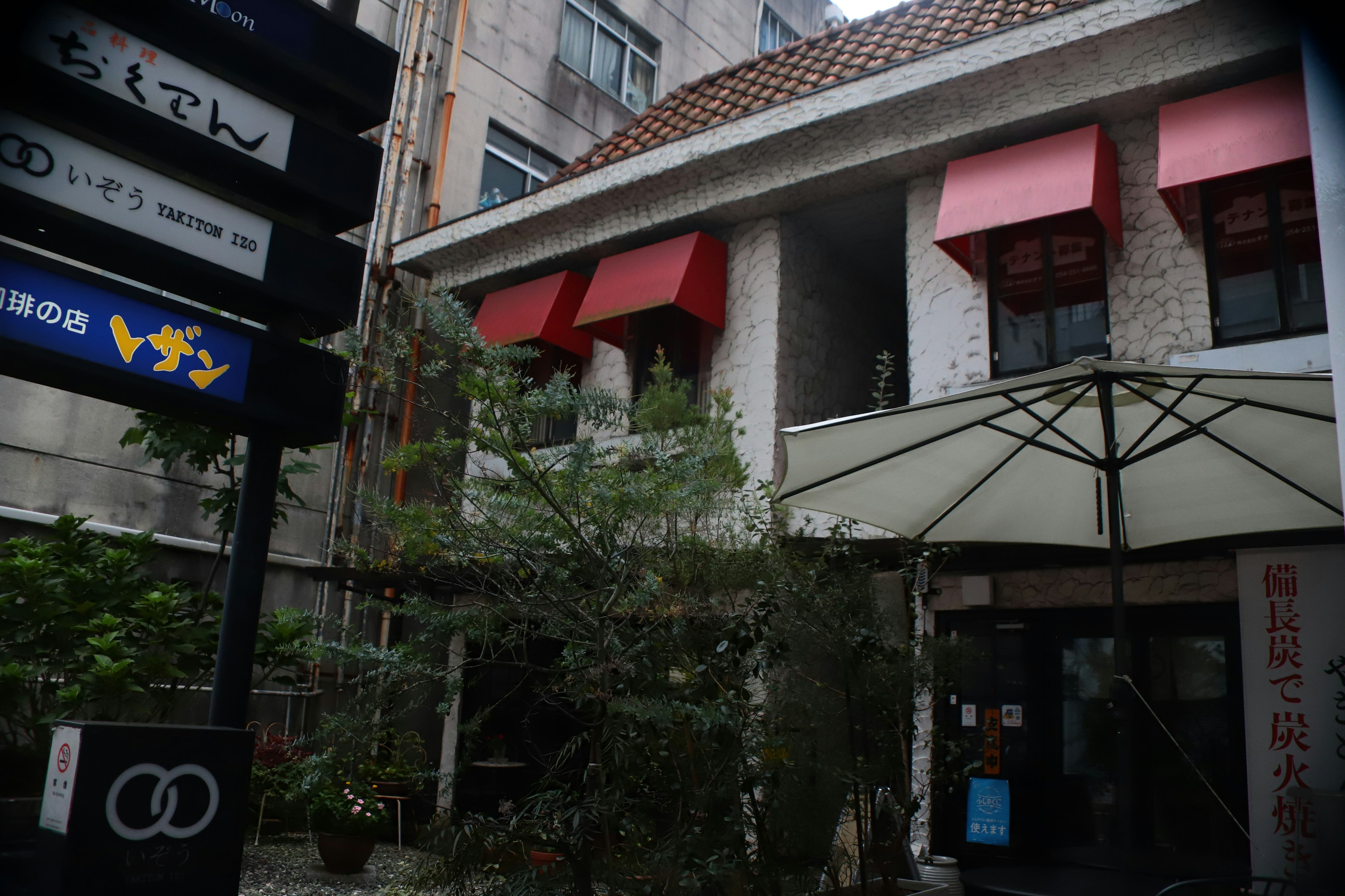 Exterior of a restaurant featuring red awnings surrounded by greenery