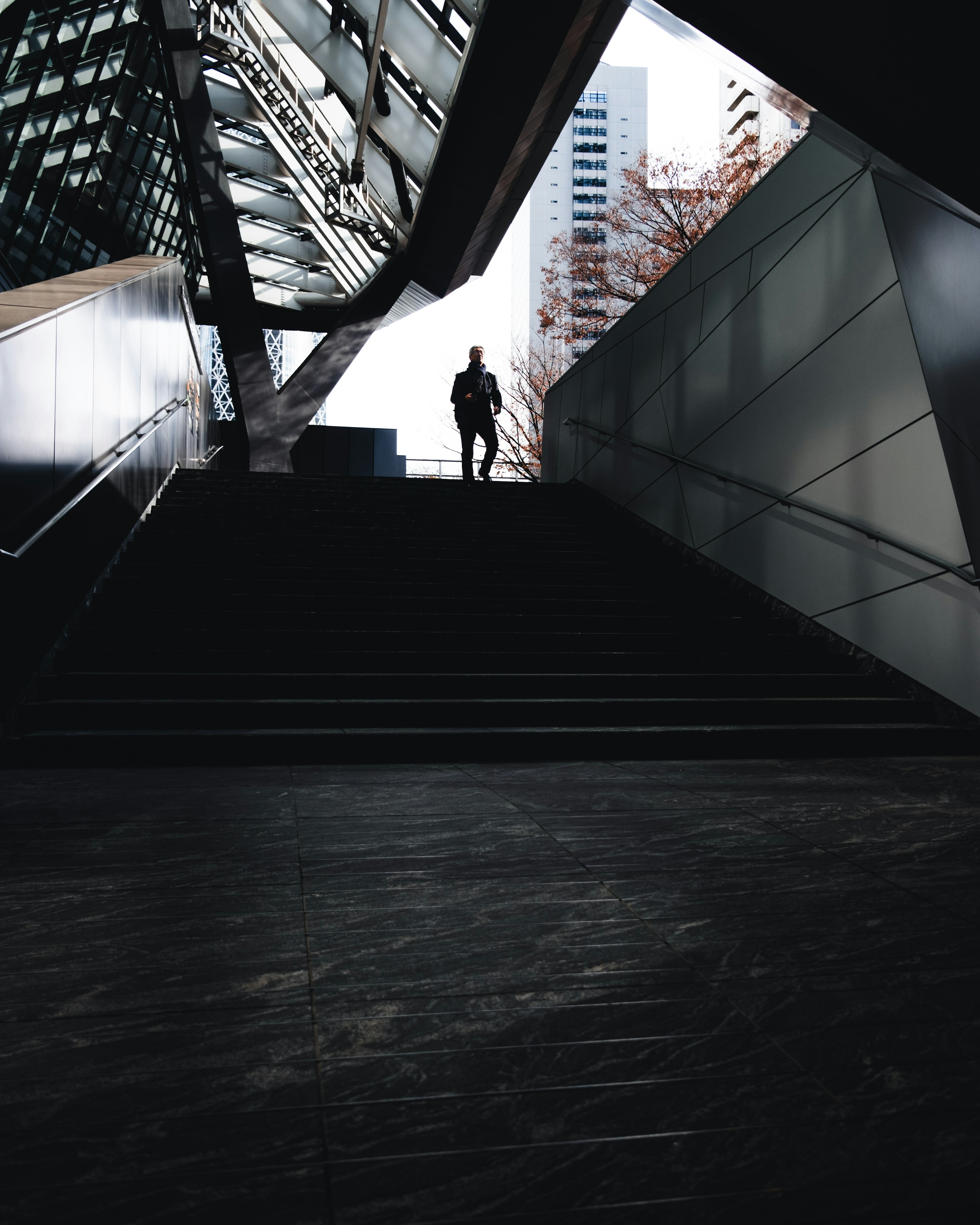 Silueta de una persona subiendo escaleras oscuras con arquitectura moderna