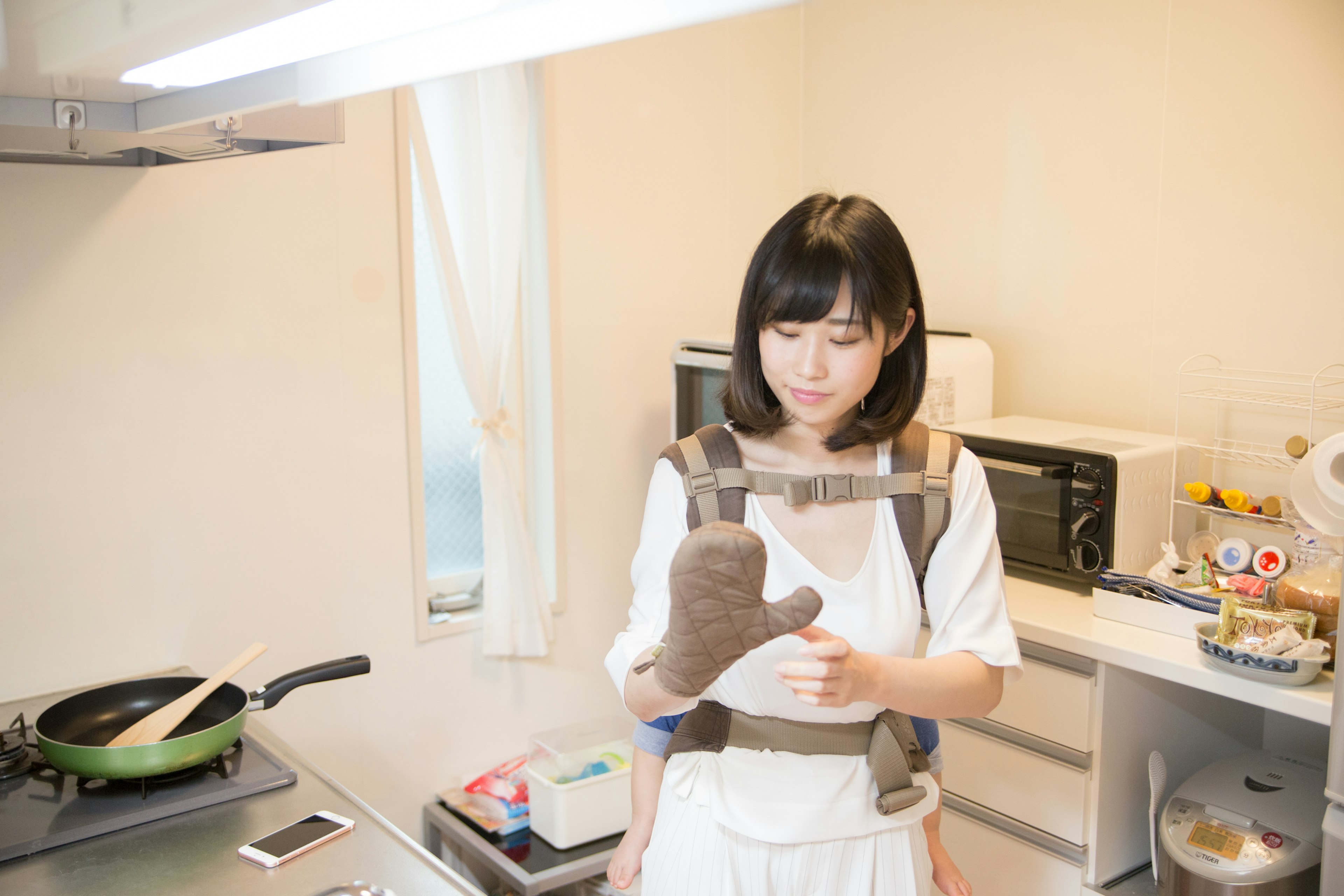 Woman in a kitchen wearing an oven mitt and preparing to cook