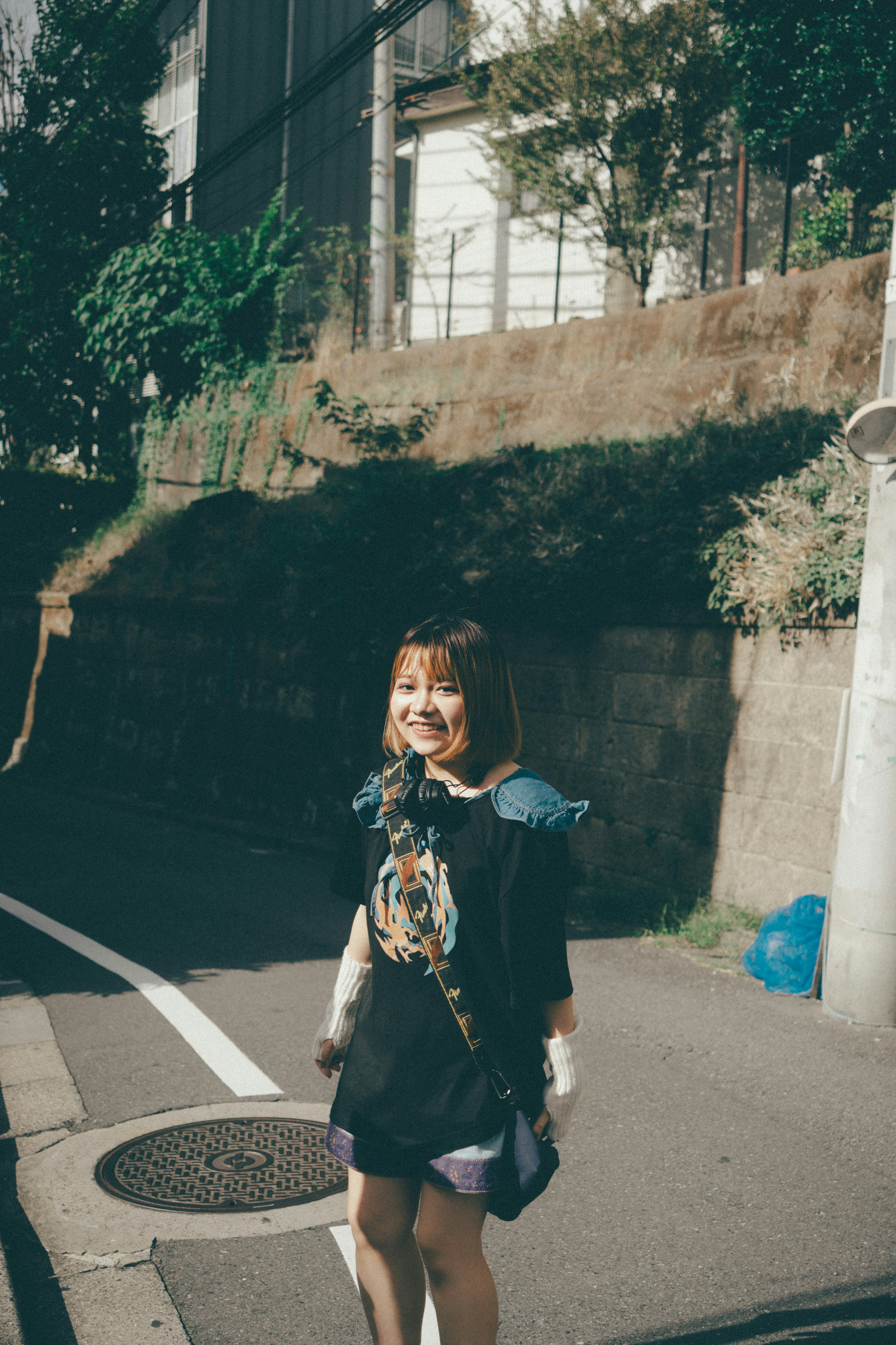 A woman smiling while standing on a street with greenery and buildings in the background