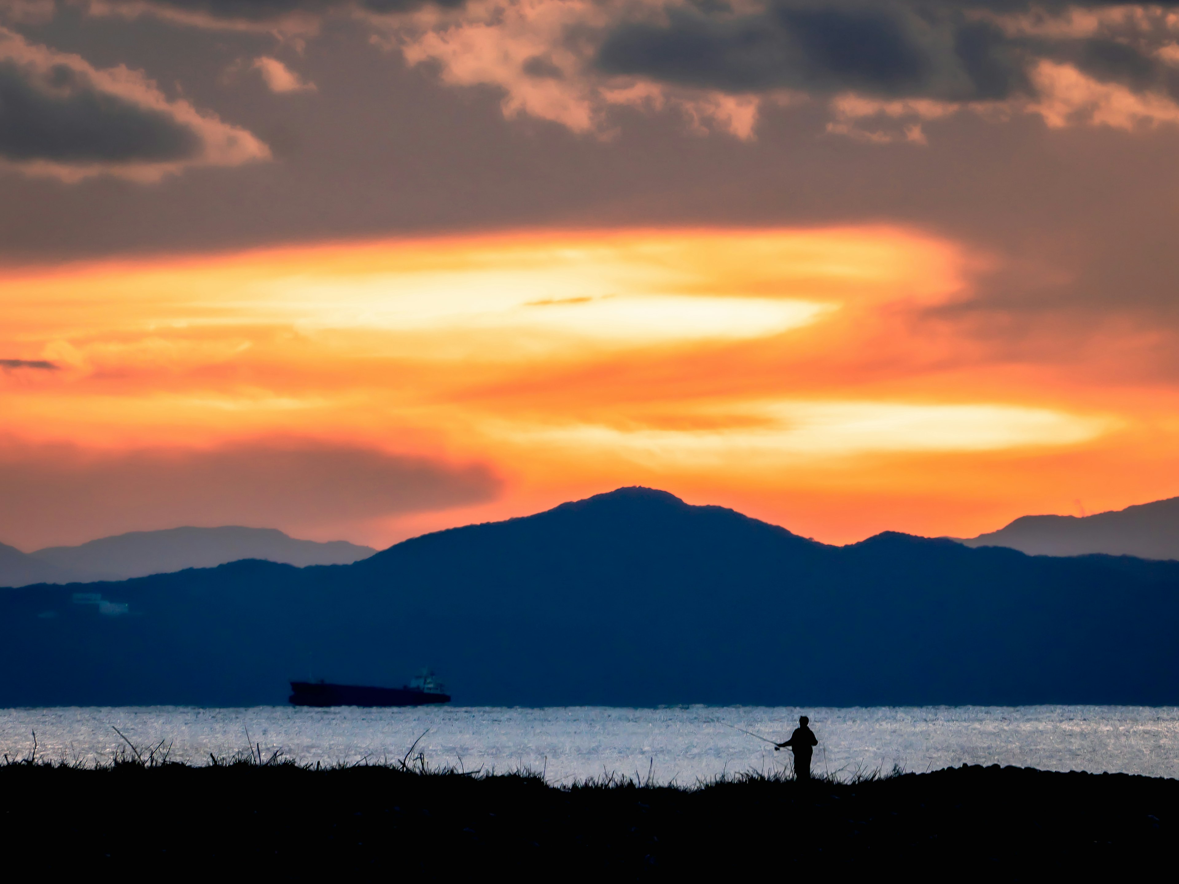 Silhouette eines Fischers vor einem schönen Sonnenuntergang über dem Meer und den Bergen