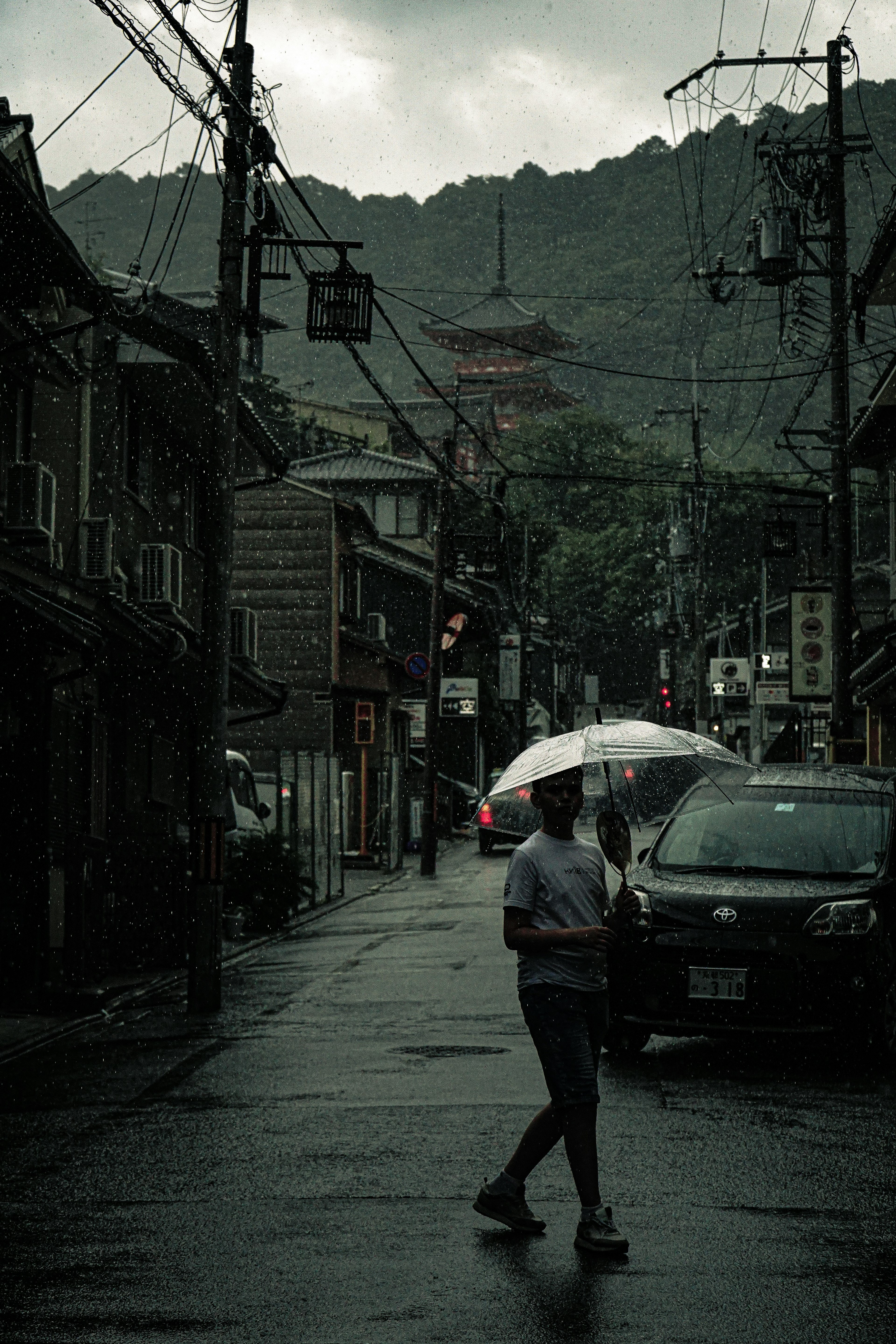 一個人在雨中撐著傘走在一條舊建築林立的街道上