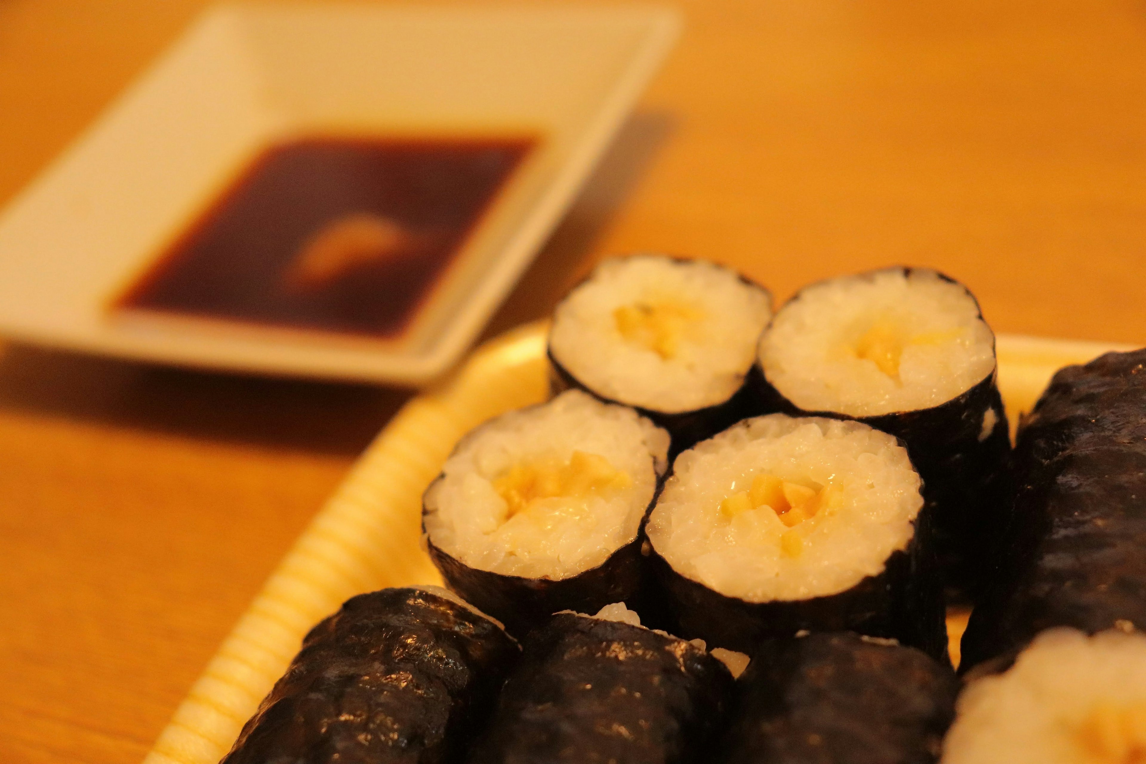 A plate of sushi rolls on a wooden table with dipping sauce