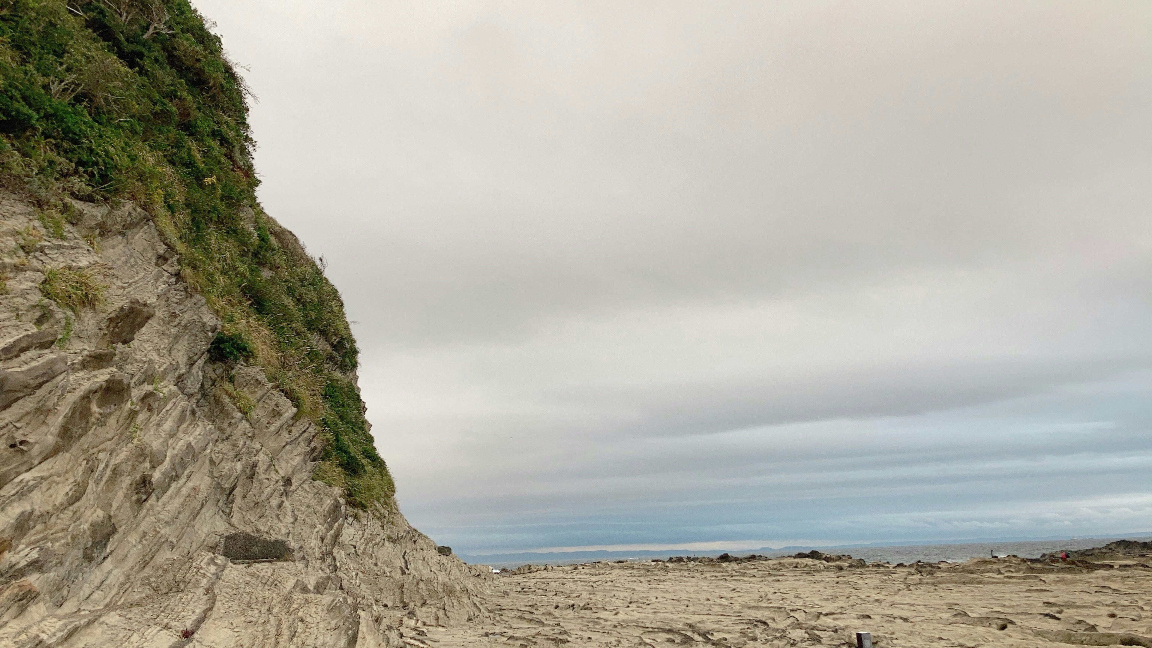 Scenic view of a green cliff against a sandy beach and ocean