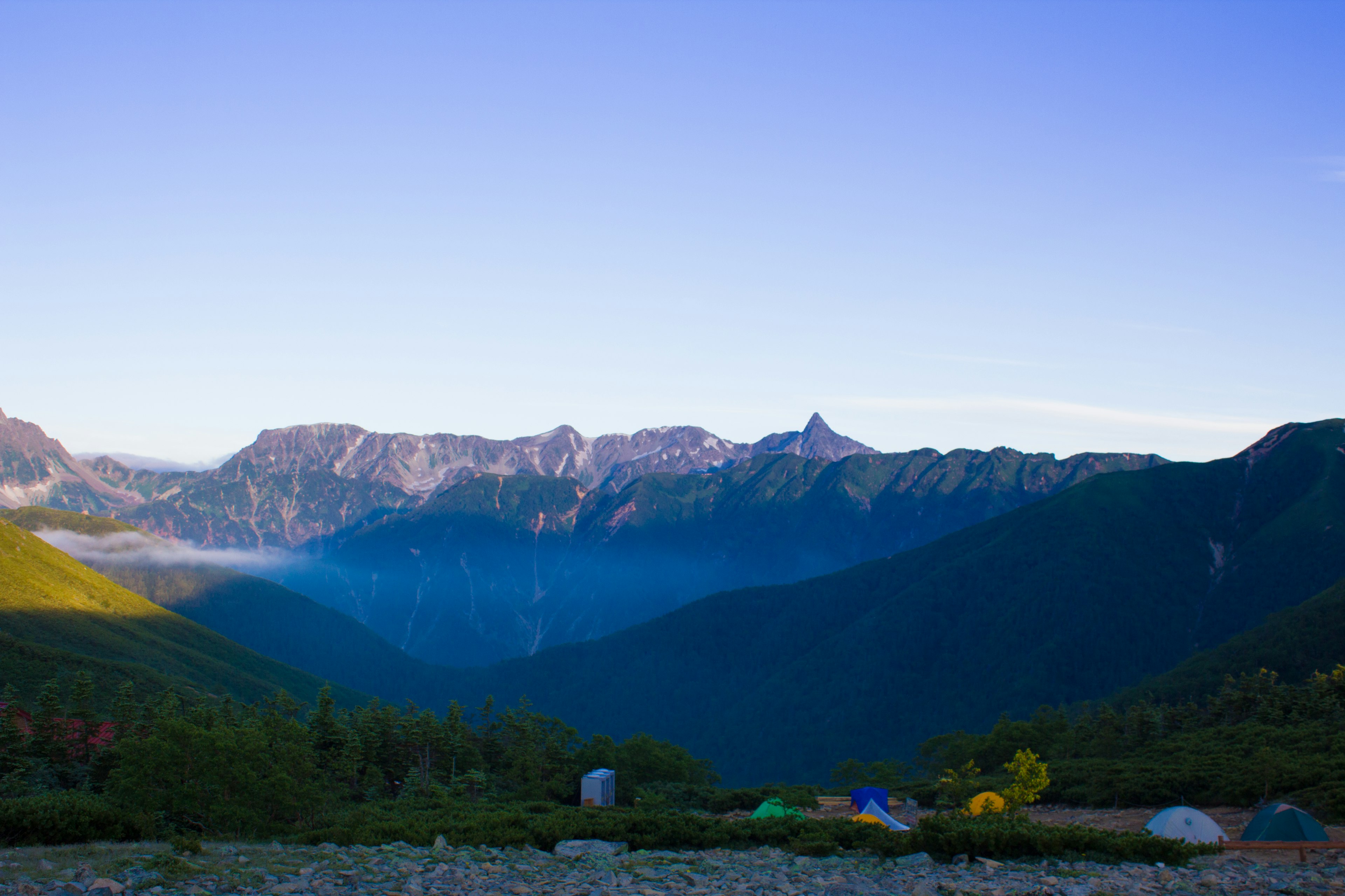 Vue panoramique des montagnes sous un ciel bleu clair avec des tentes de camping visibles