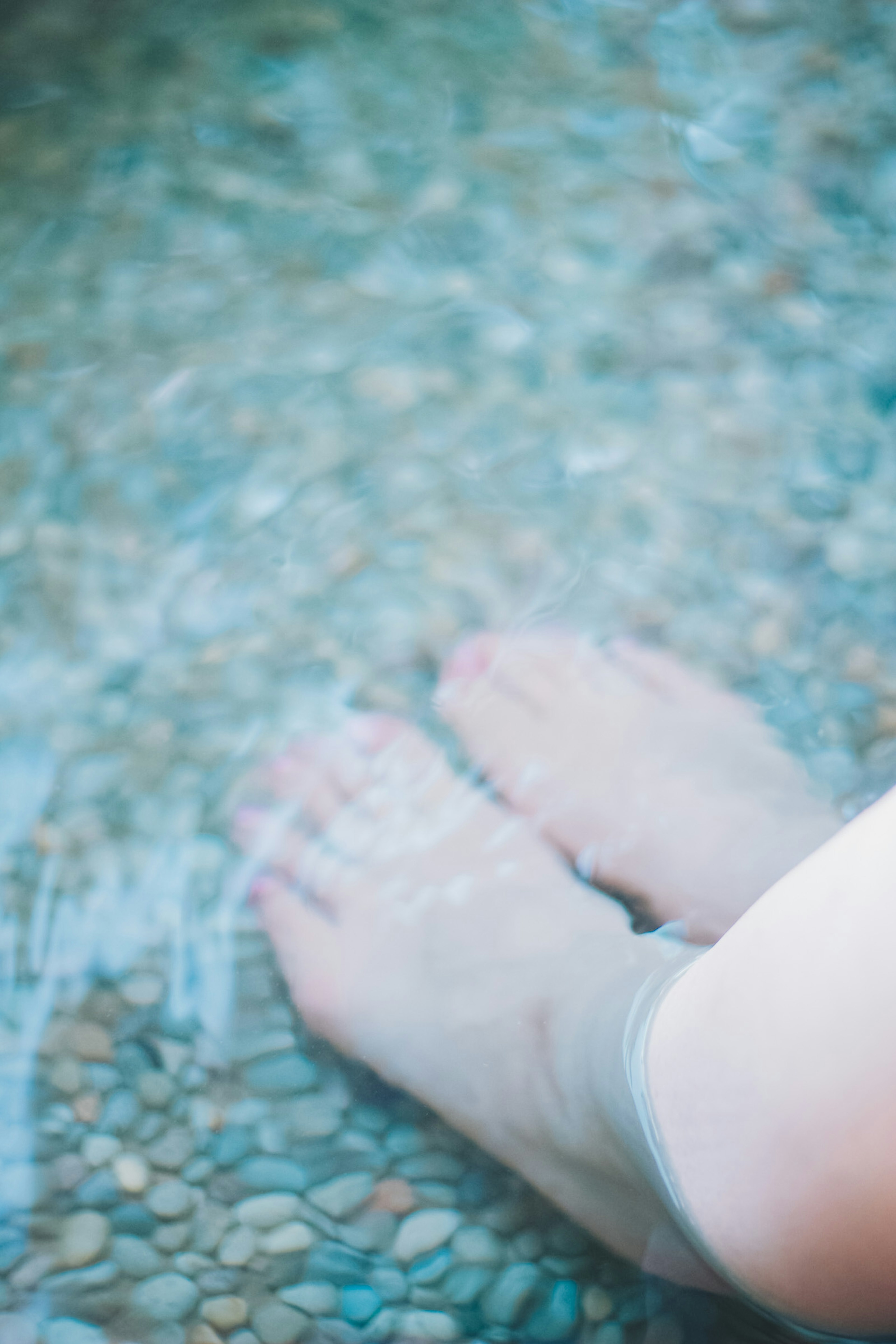 Piedi immersi nell'acqua con ciottoli sottostanti