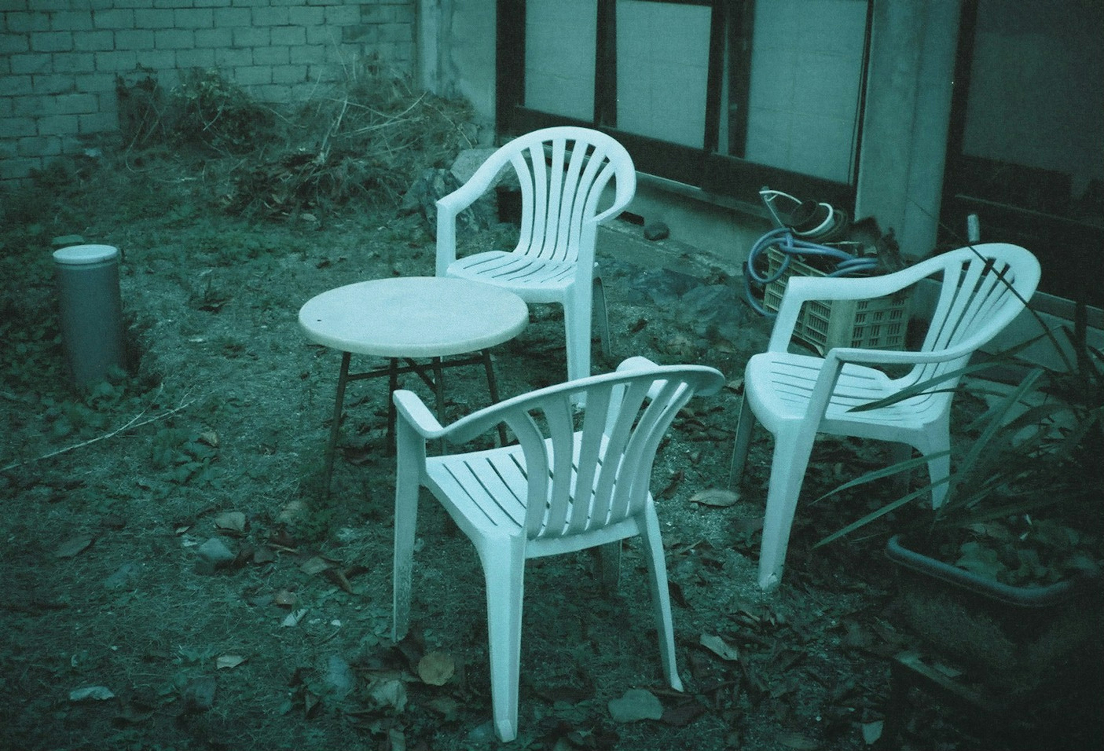 A scene of a messy garden with white plastic chairs and a table