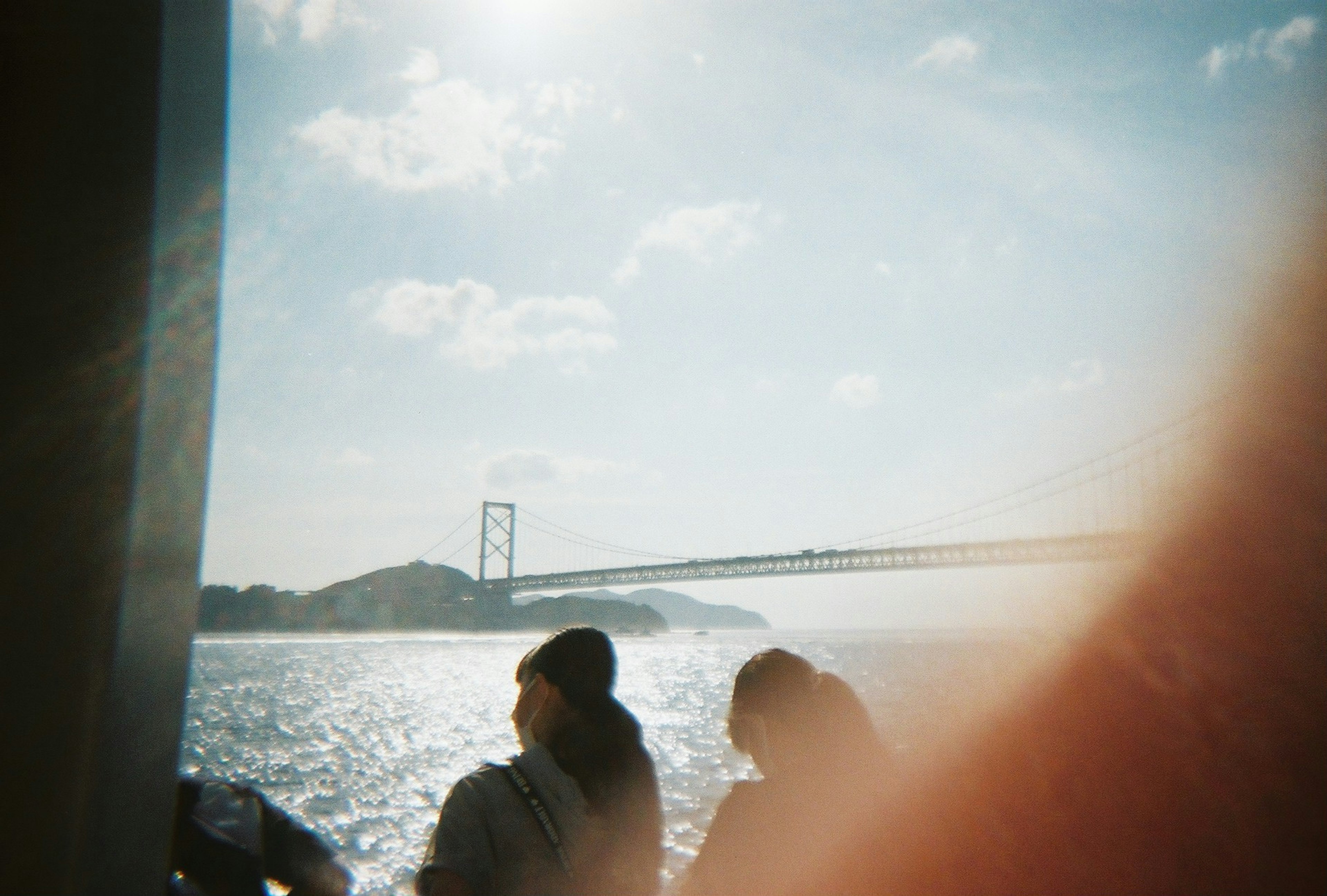 Silhouettes of people against a shimmering sea and bridge