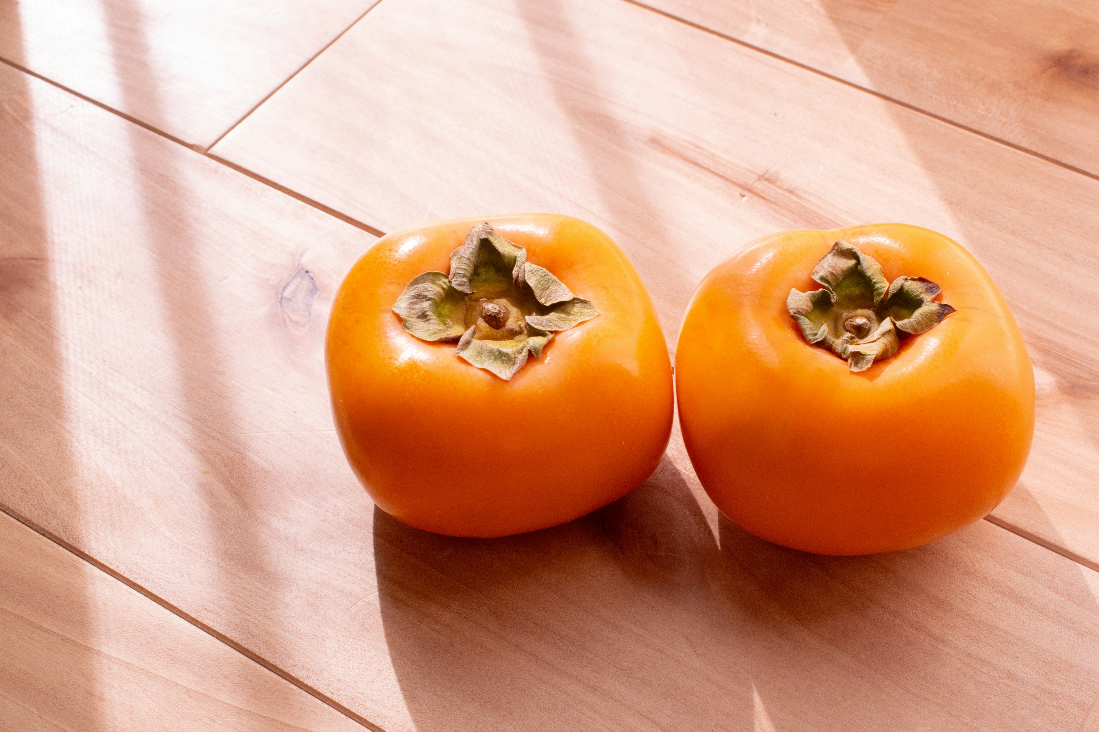 Two orange persimmons on a wooden floor