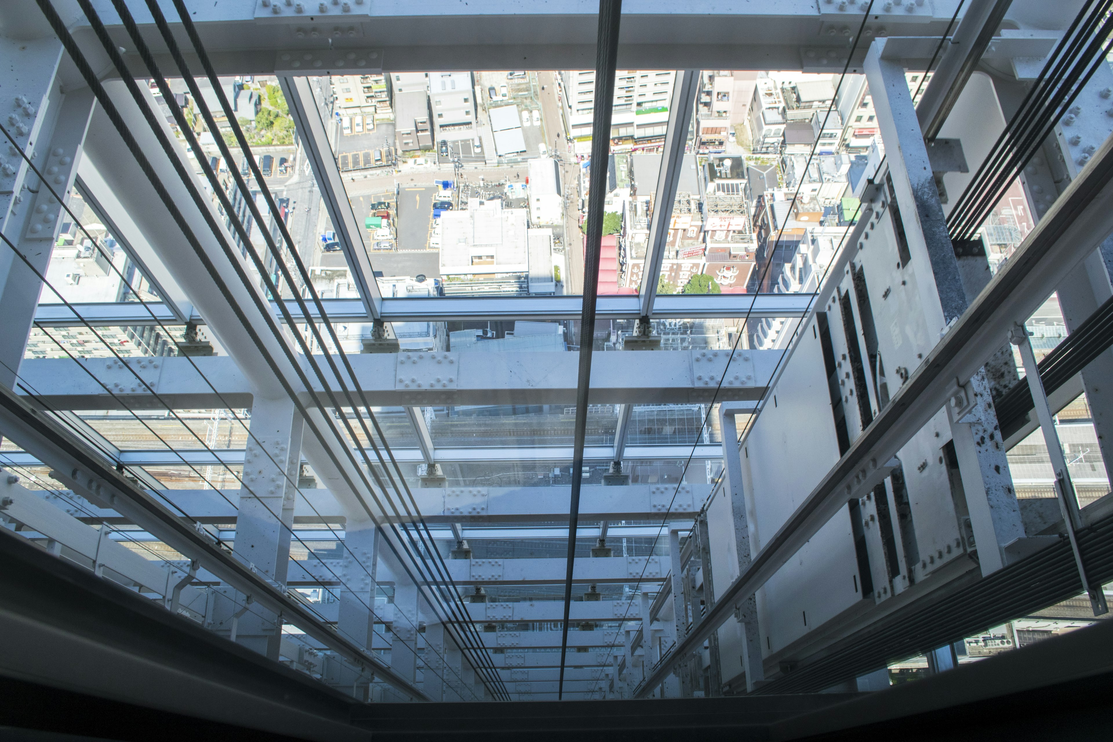 Blick nach unten durch einen Glaspersonenaufzug auf die Stadtlandschaft