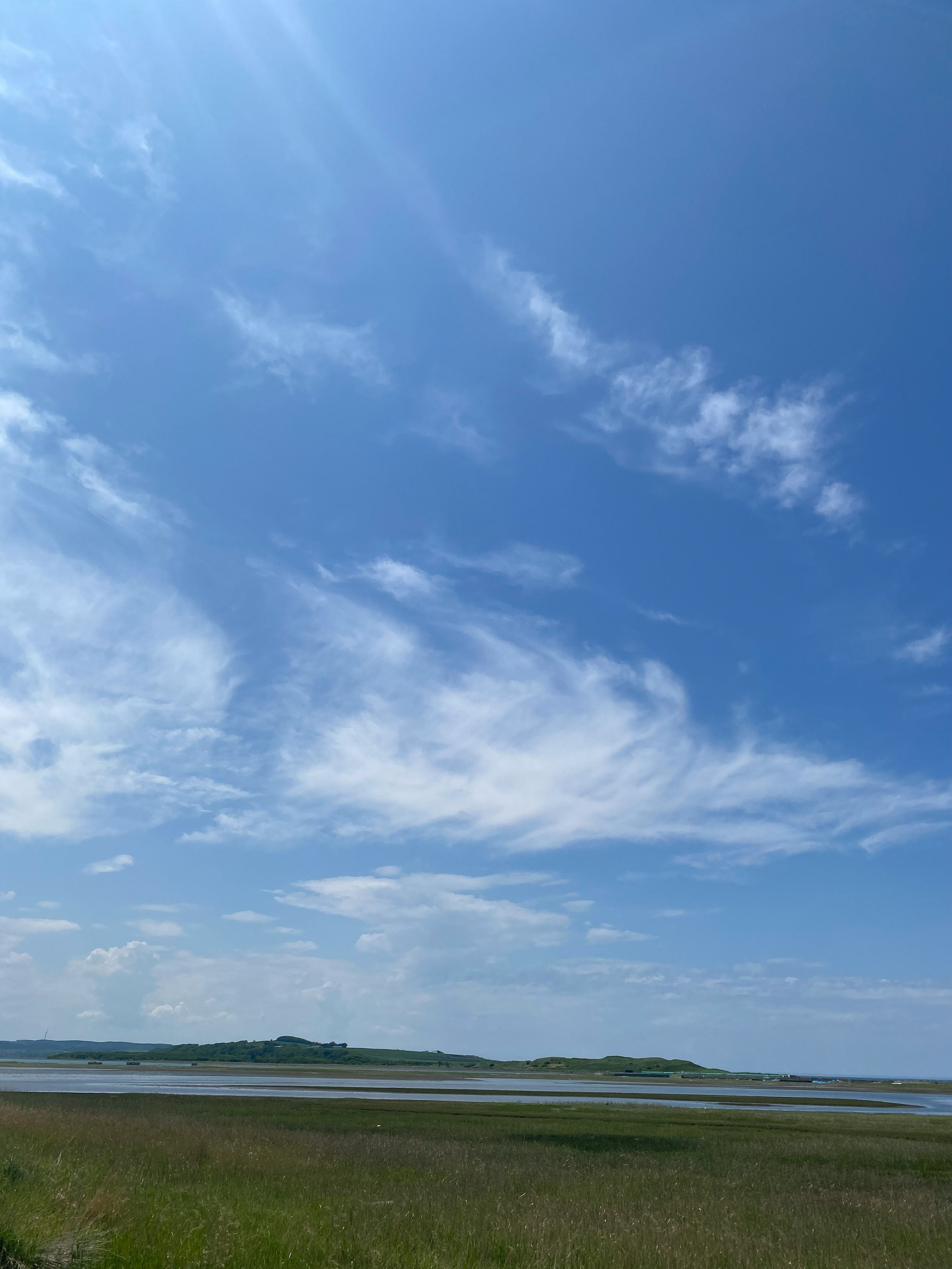 A landscape featuring a blue sky with white clouds green grass and distant islands