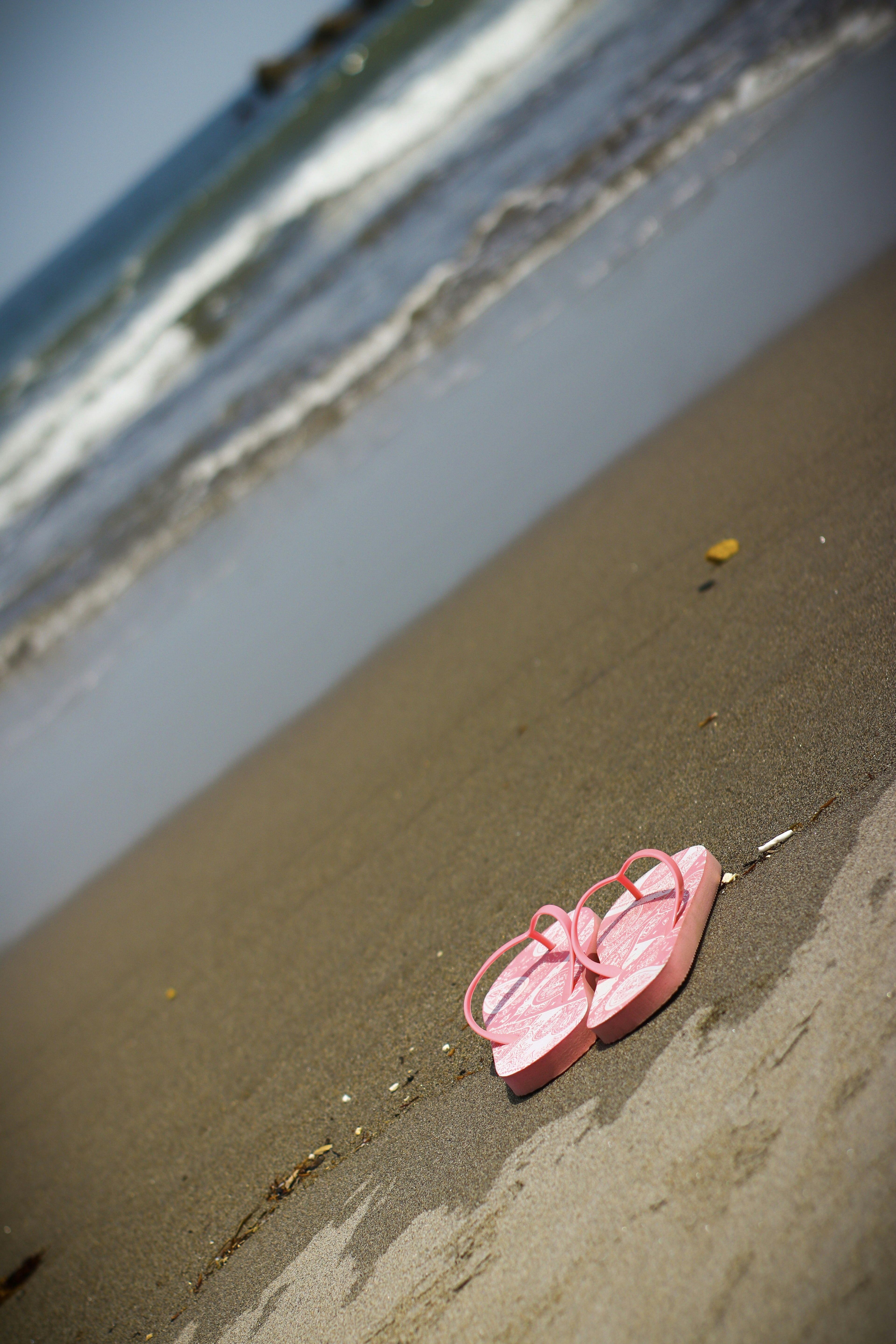 Sandalnya berwarna pink yang ditinggalkan di pantai dengan ombak di latar belakang