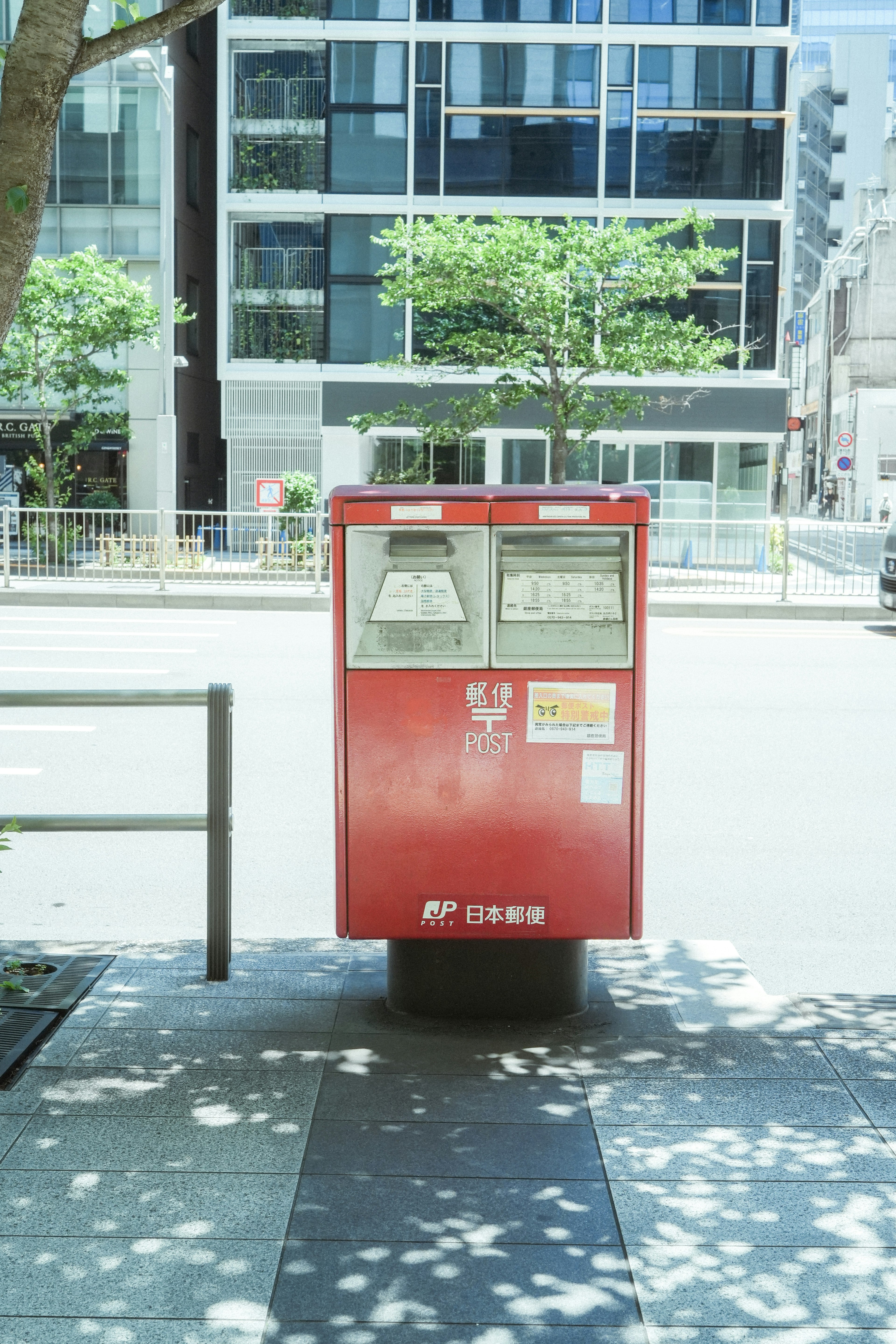 Ein roter Briefkasten steht auf der Straße mit modernen Gebäuden im Hintergrund