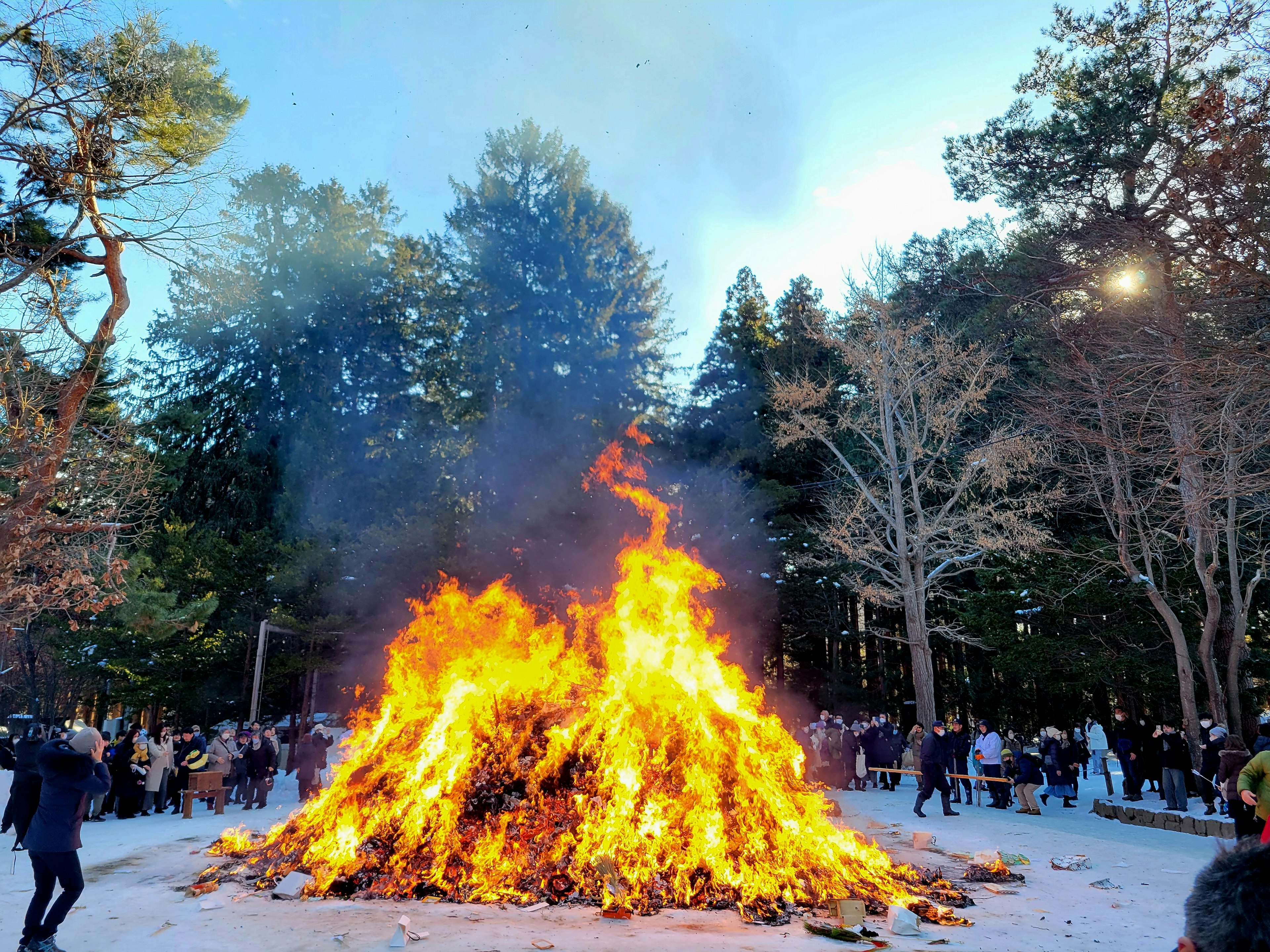 A large bonfire burning brightly with people gathered around in a winter festival setting