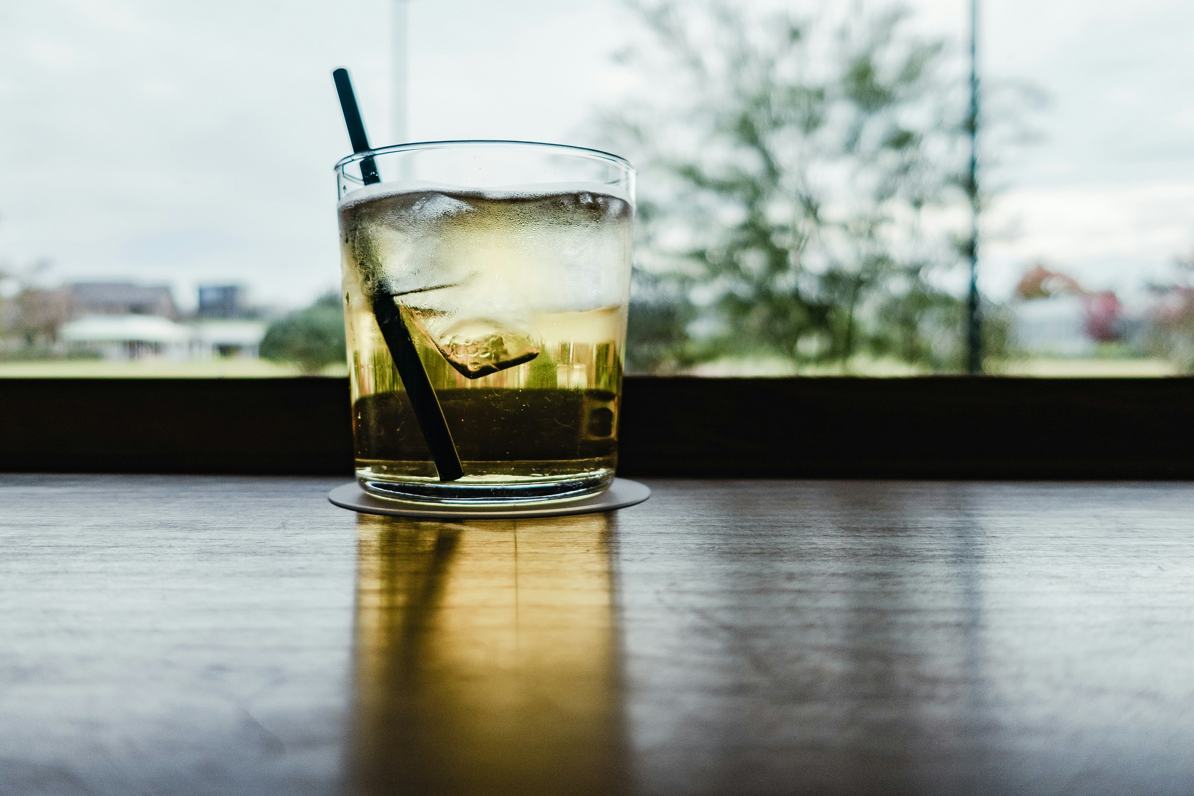 Cocktailglas mit Eis auf einem Holztisch am Fenster