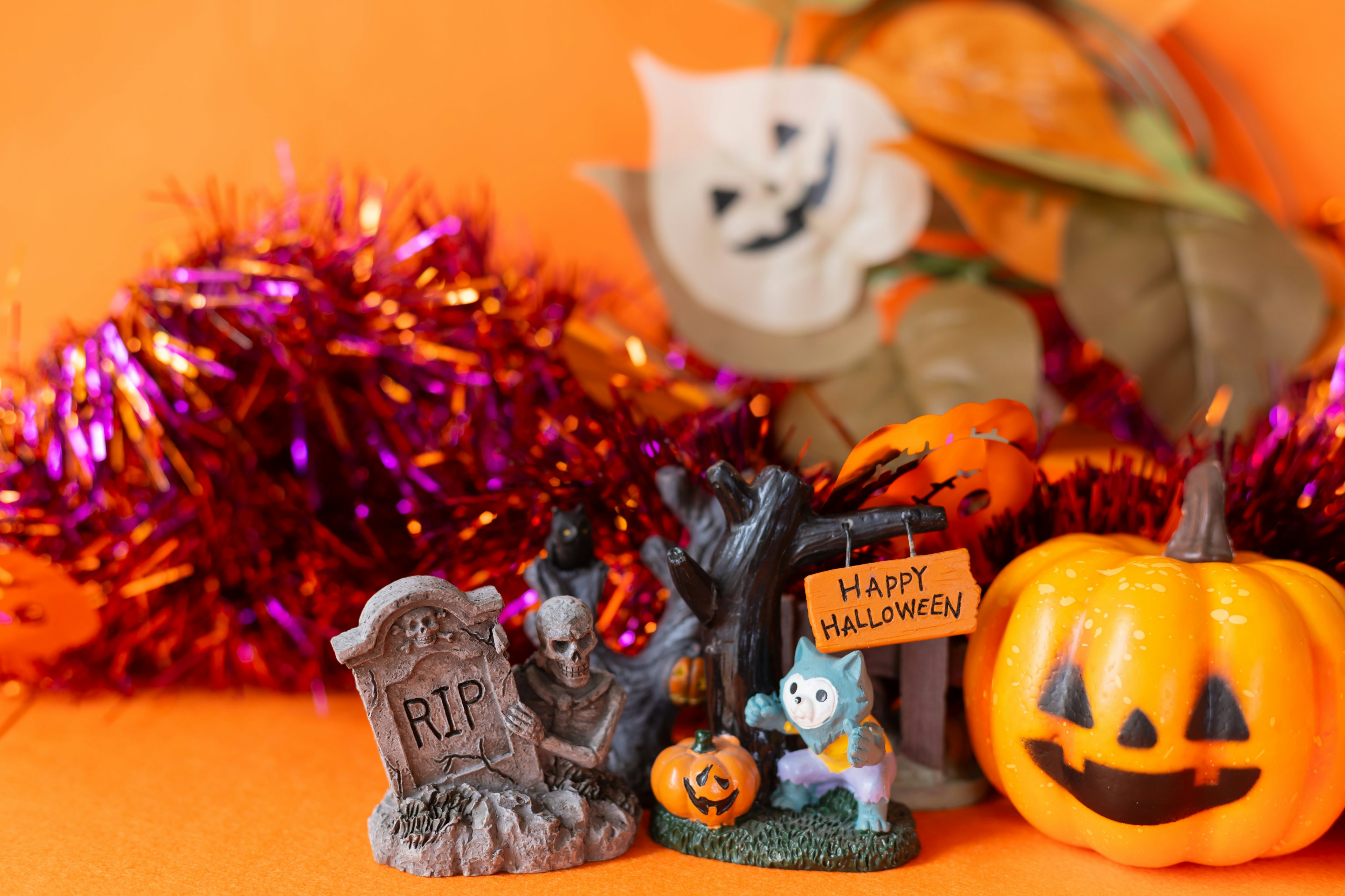 Halloween decorations featuring a pumpkin a gravestone and a ghost on an orange background