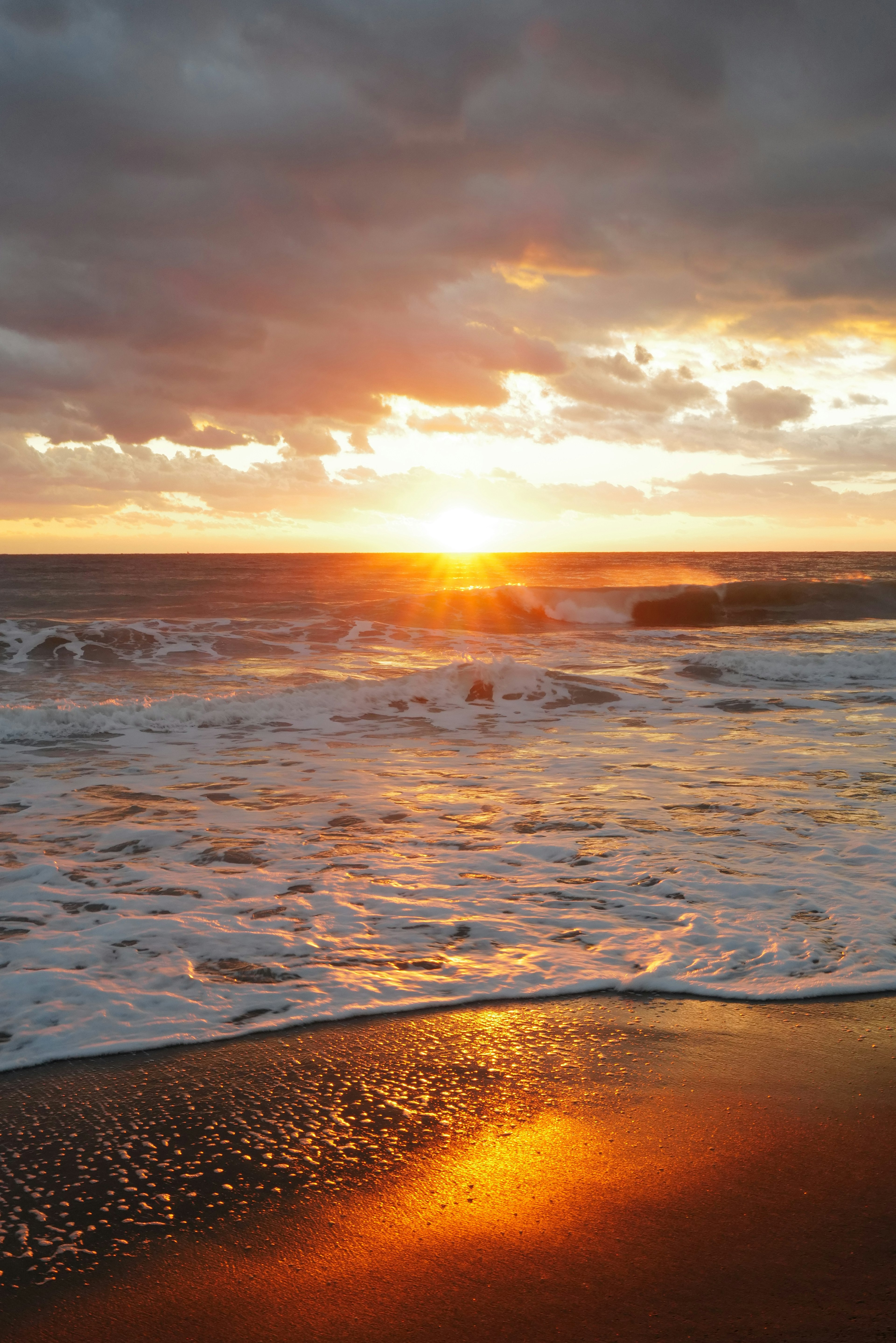 Vista escénica de una playa con olas y un atardecer reflejándose en el agua