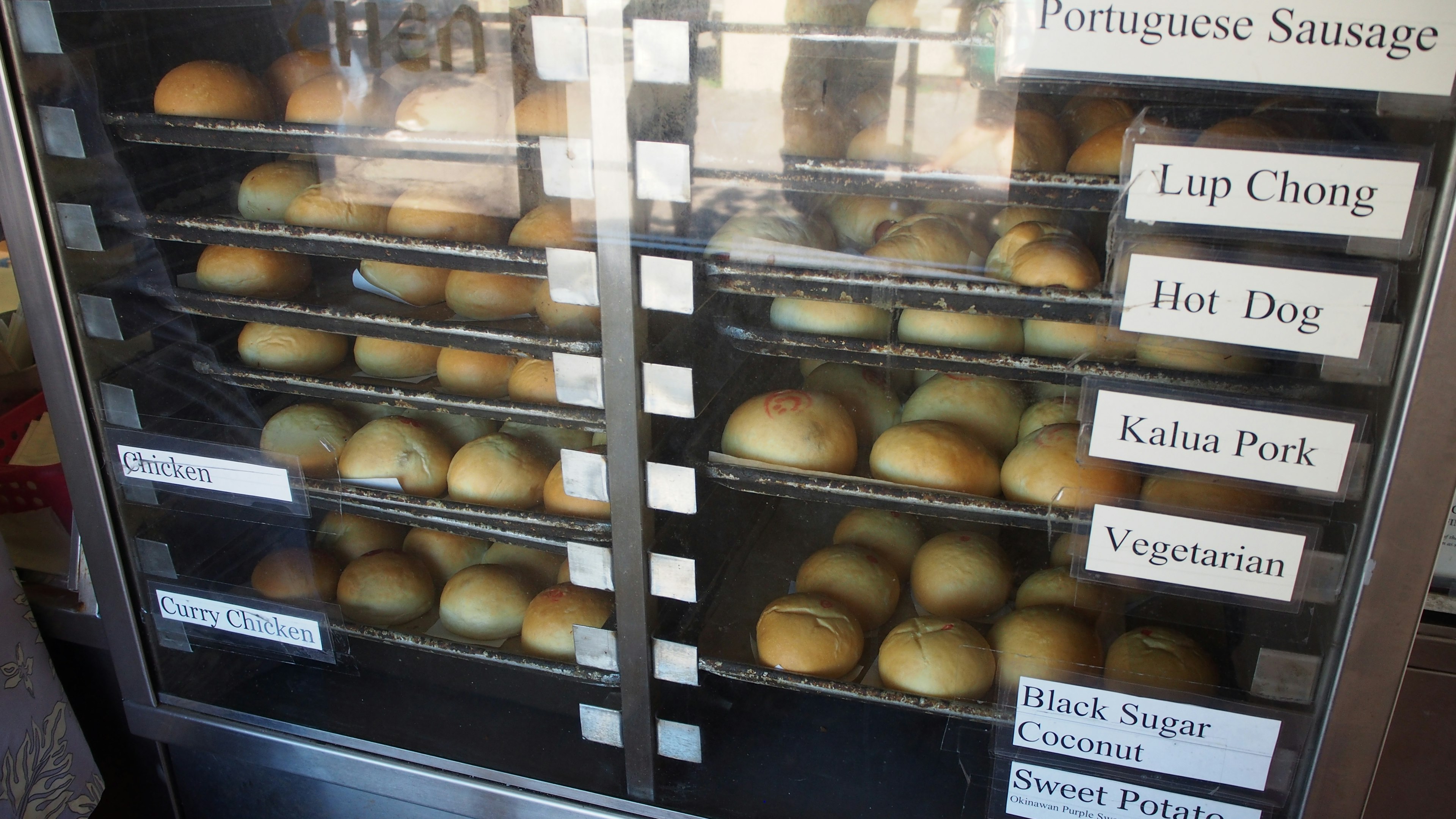 Display case filled with various types of buns including hot dogs and Portuguese sausage