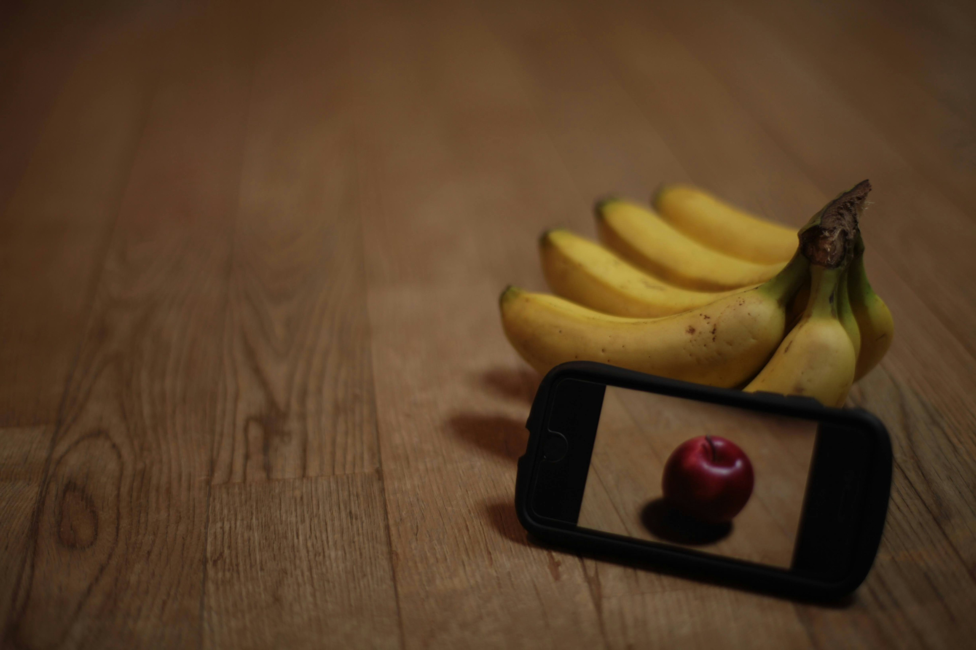 Un grappolo di banane accanto a uno smartphone che mostra una mela