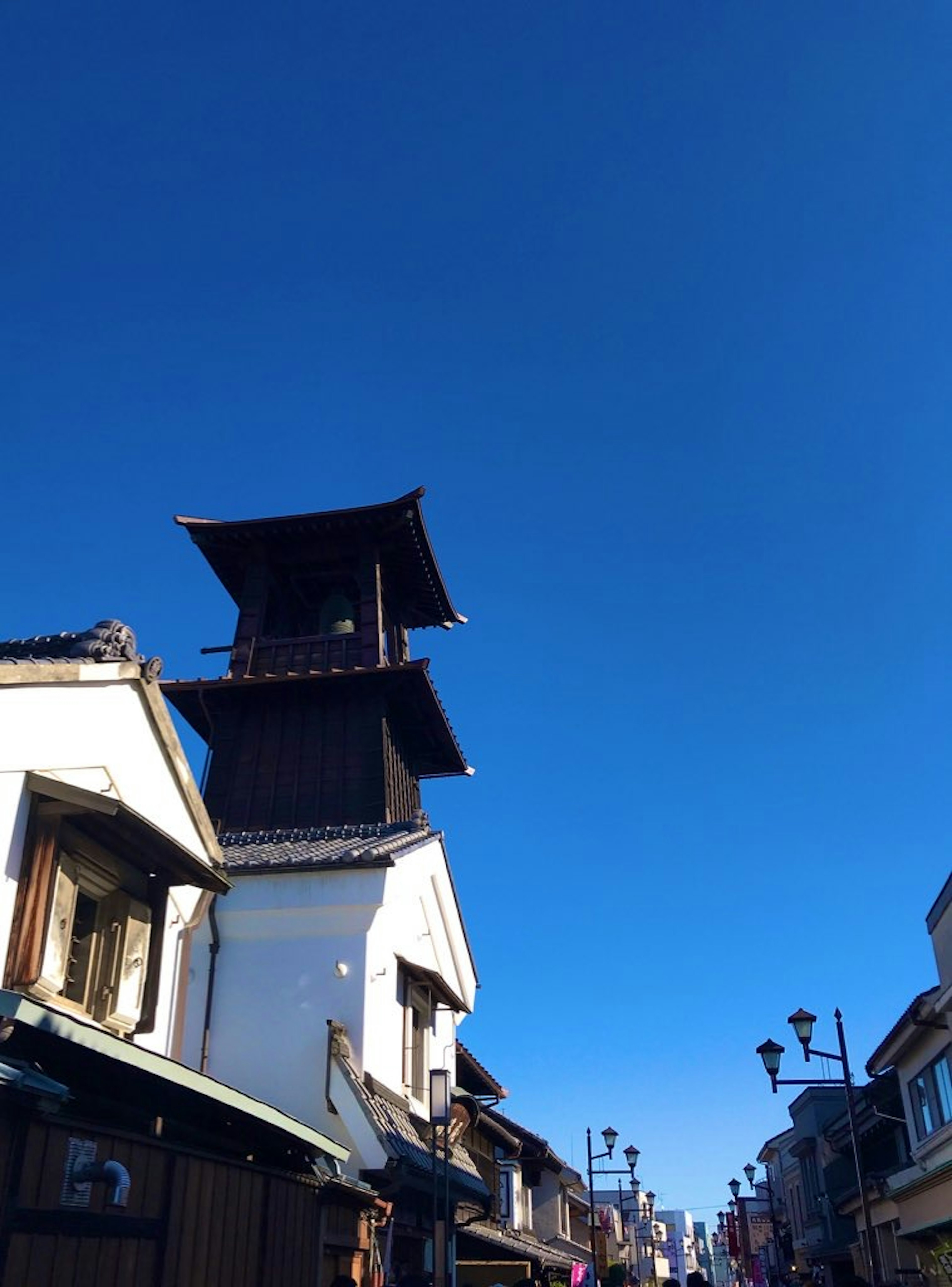 Menara jam tradisional Jepang menjulang di bawah langit biru cerah dengan jalan bersejarah