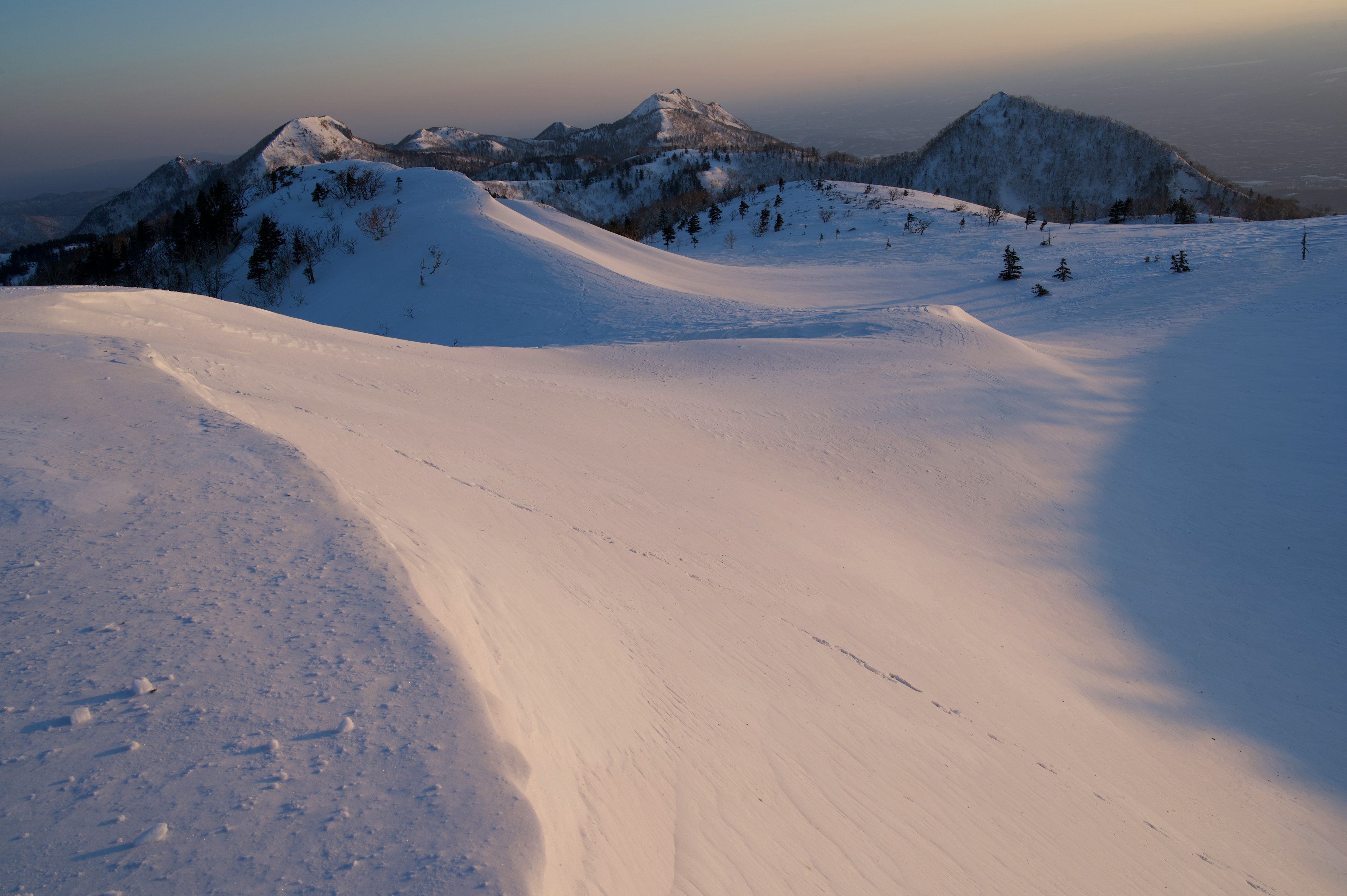 雪に覆われた山々の風景と柔らかな夕暮れの光