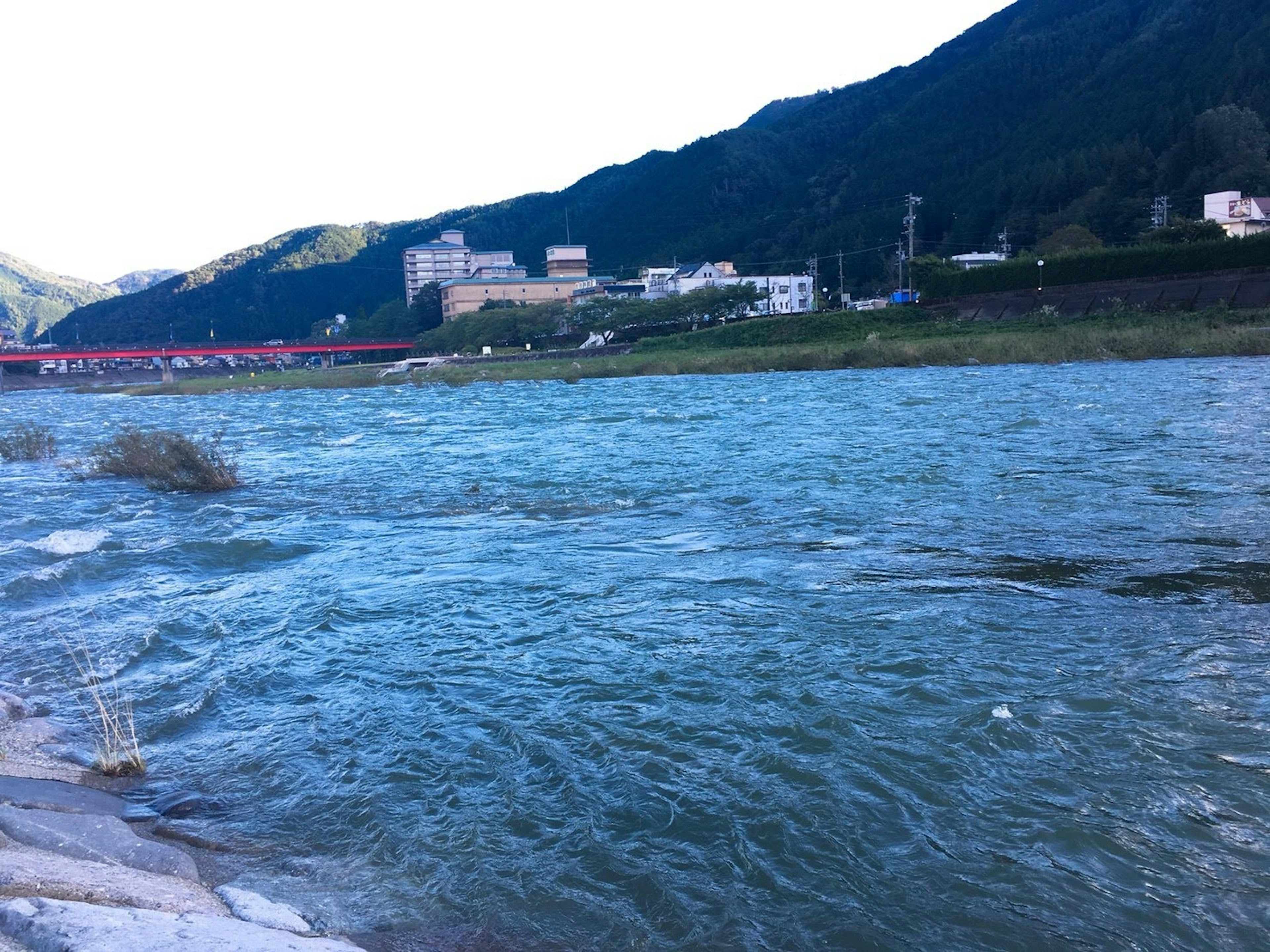 Ein fließender Fluss mit Bergen im Hintergrund und Gebäuden am Ufer